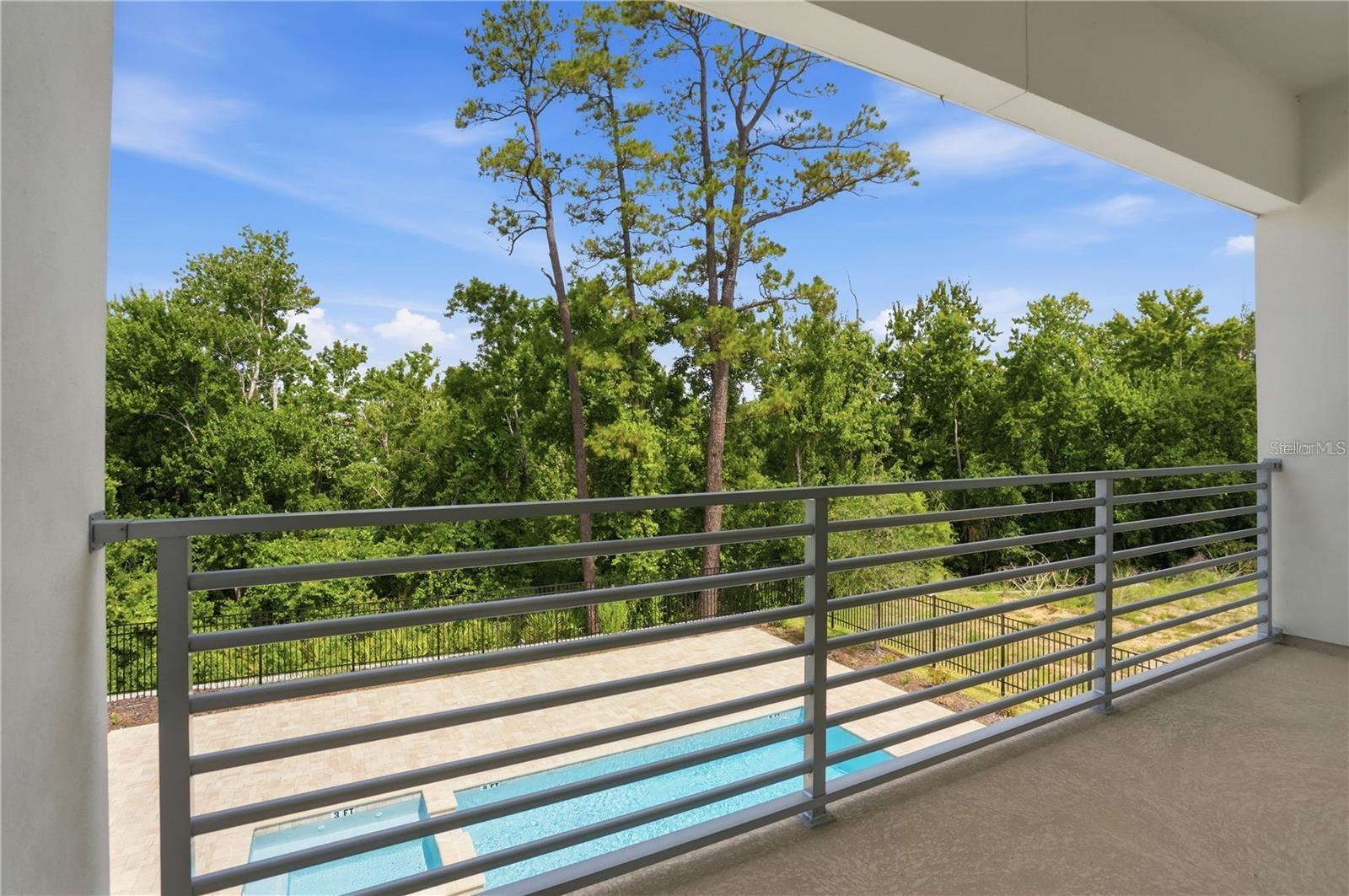 Covered balcony overlooking a swimming pool and dense trees.