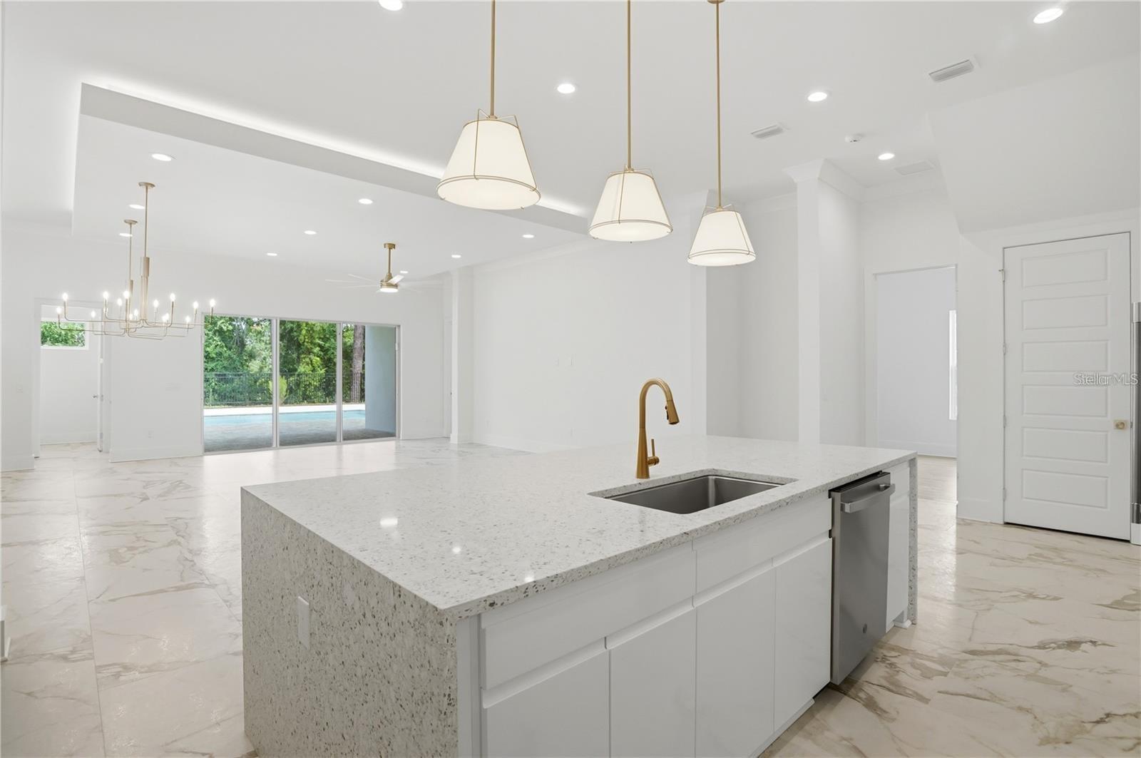 Open-plan kitchen with a large stone island, gold faucet, and sliding doors to a pool patio.