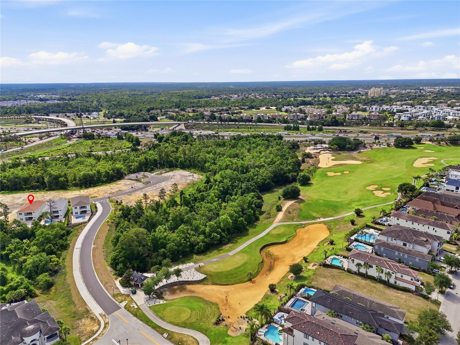 Aerial view of a golf course, surrounding homes, and a red marker on one property.