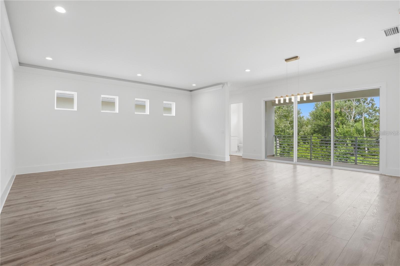 Empty living room with gray plank flooring and sliding glass doors to a tree-lined balcony.