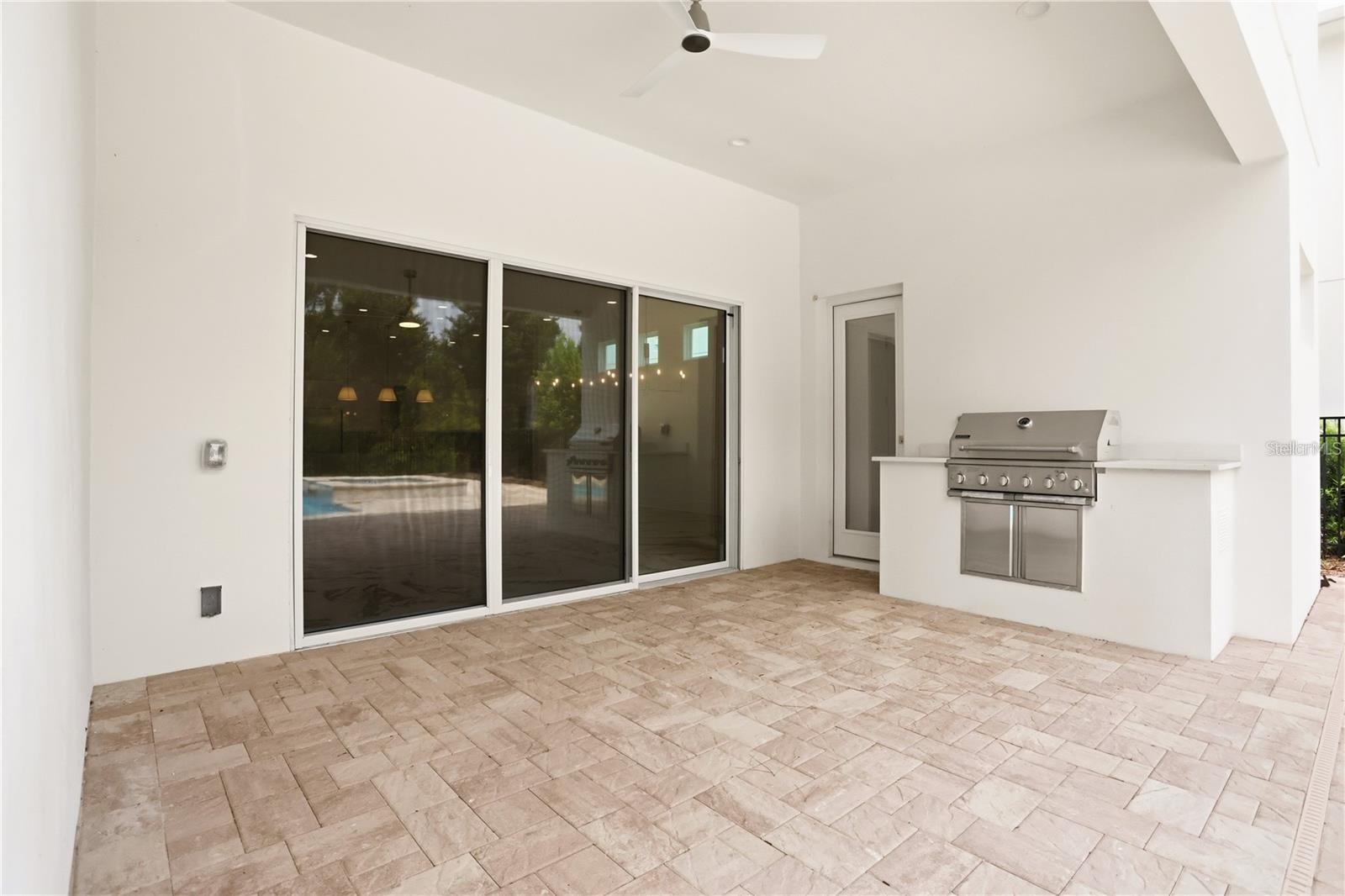 Covered patio with stone pavers, sliding glass doors, and a built-in stainless steel grill.