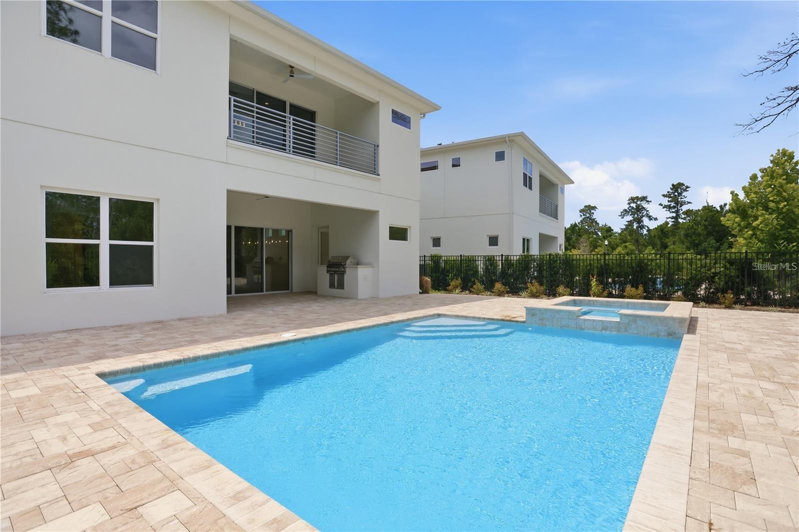 Modern white home beside a blue swimming pool with a raised spa and paved patio.