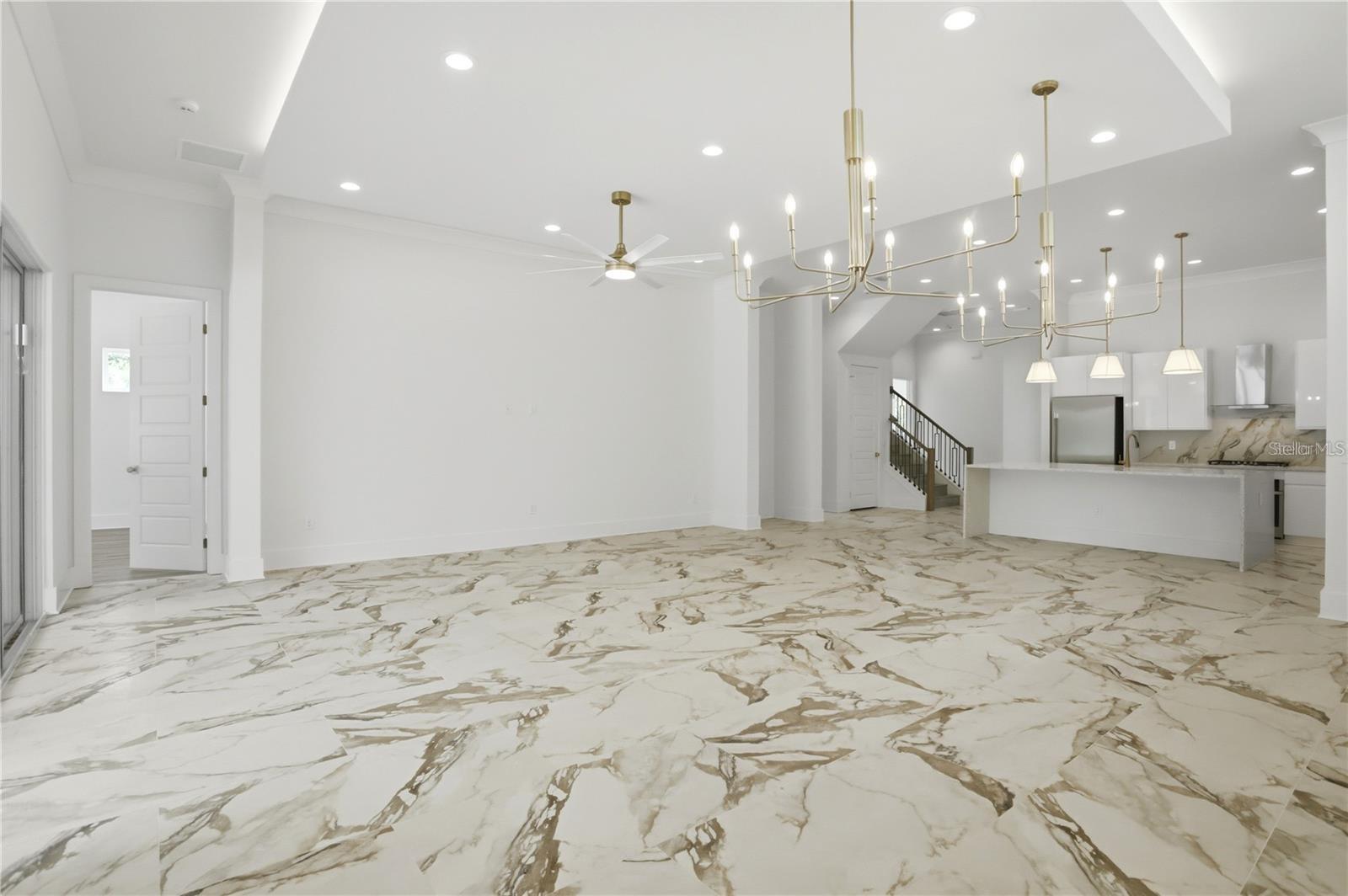Vacant open-plan dining area with dramatic veined flooring, gold chandeliers, and an adjoining white kitchen.