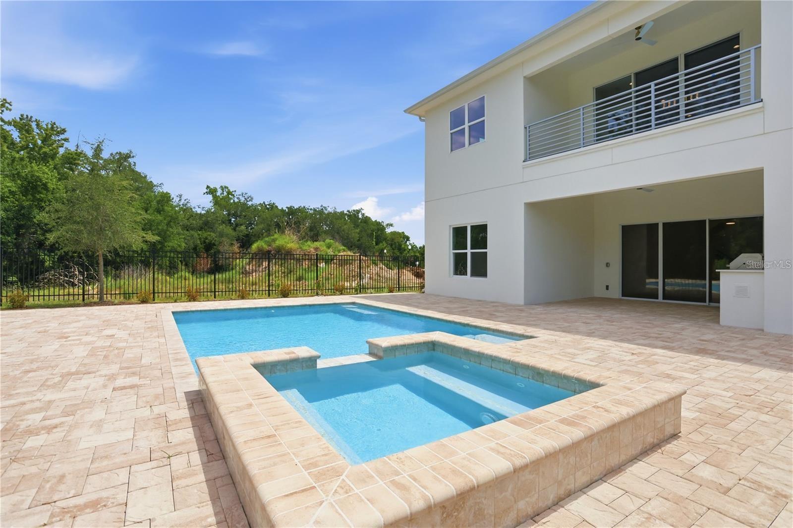 Modern home with a backyard pool and raised spa beside a tiled patio and upper balcony.