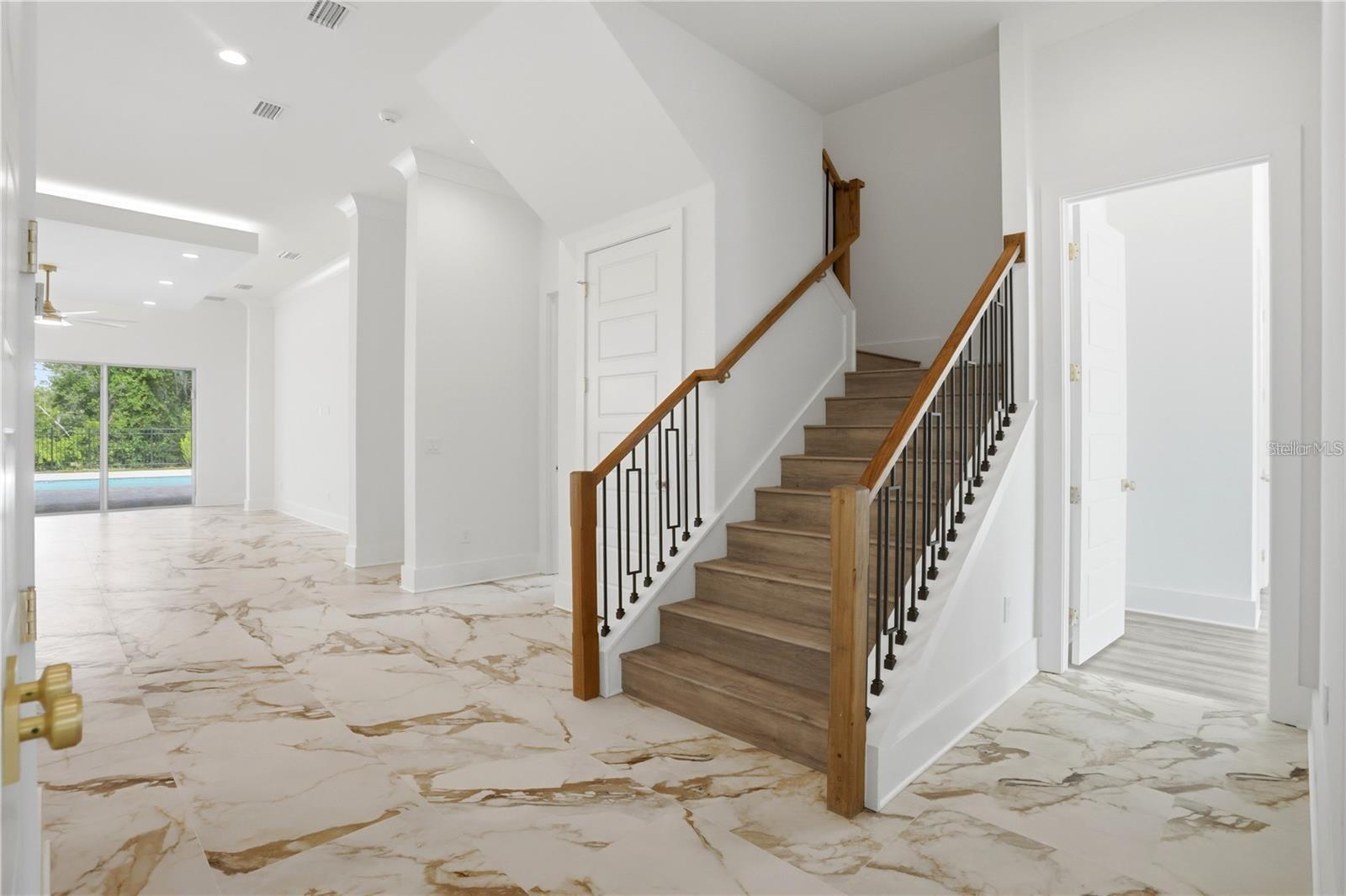 Entry foyer with a wood staircase, black balusters, and marble-look tile flooring.