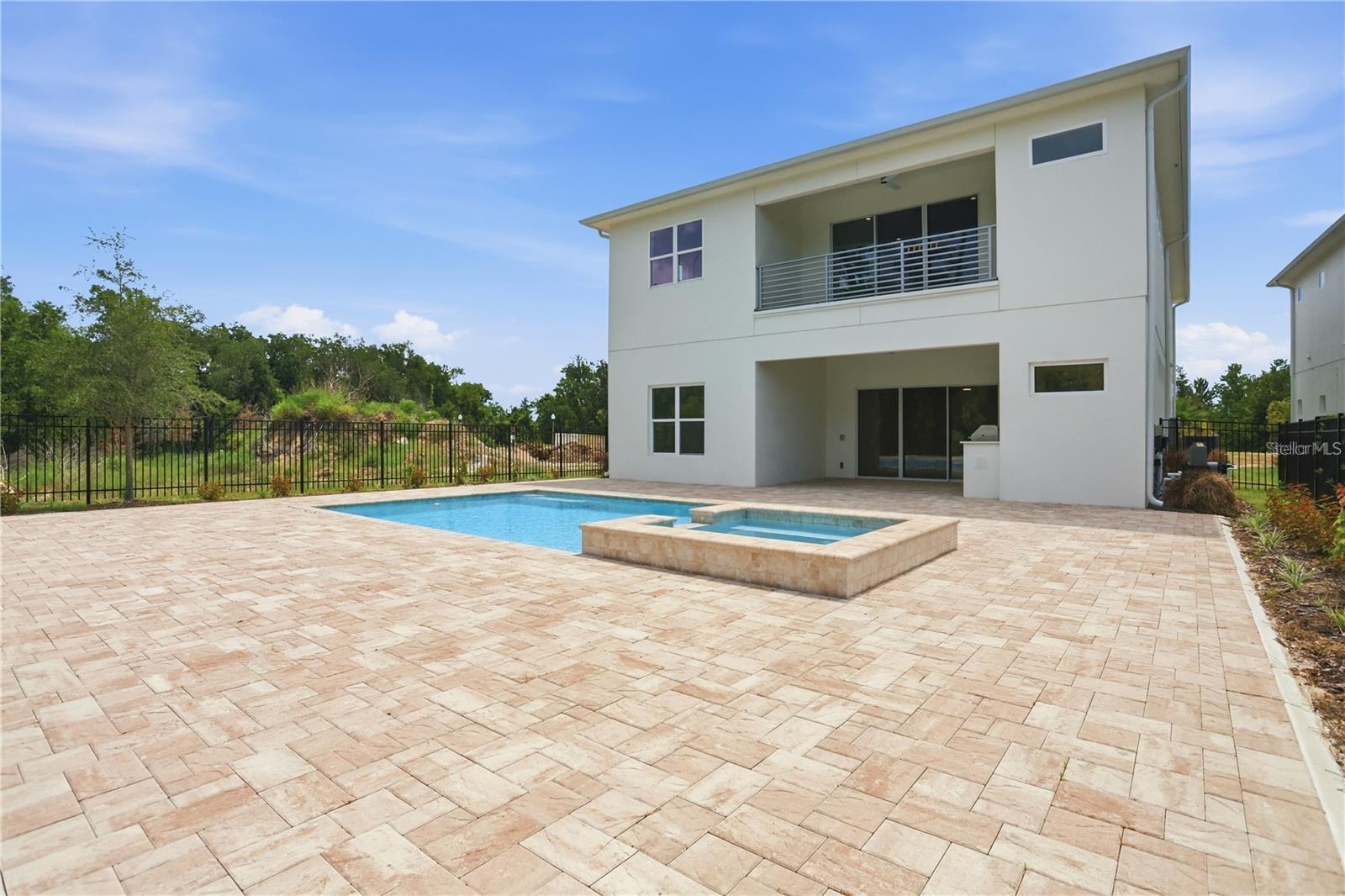 Modern two-story home with a paved pool terrace, raised spa, and upper balcony.