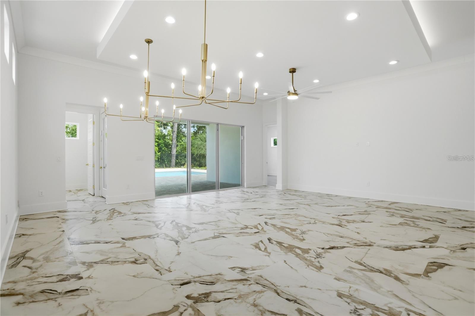 Bright, vacant dining room with marble-pattern flooring, a brass chandelier, and sliding doors to a pool.