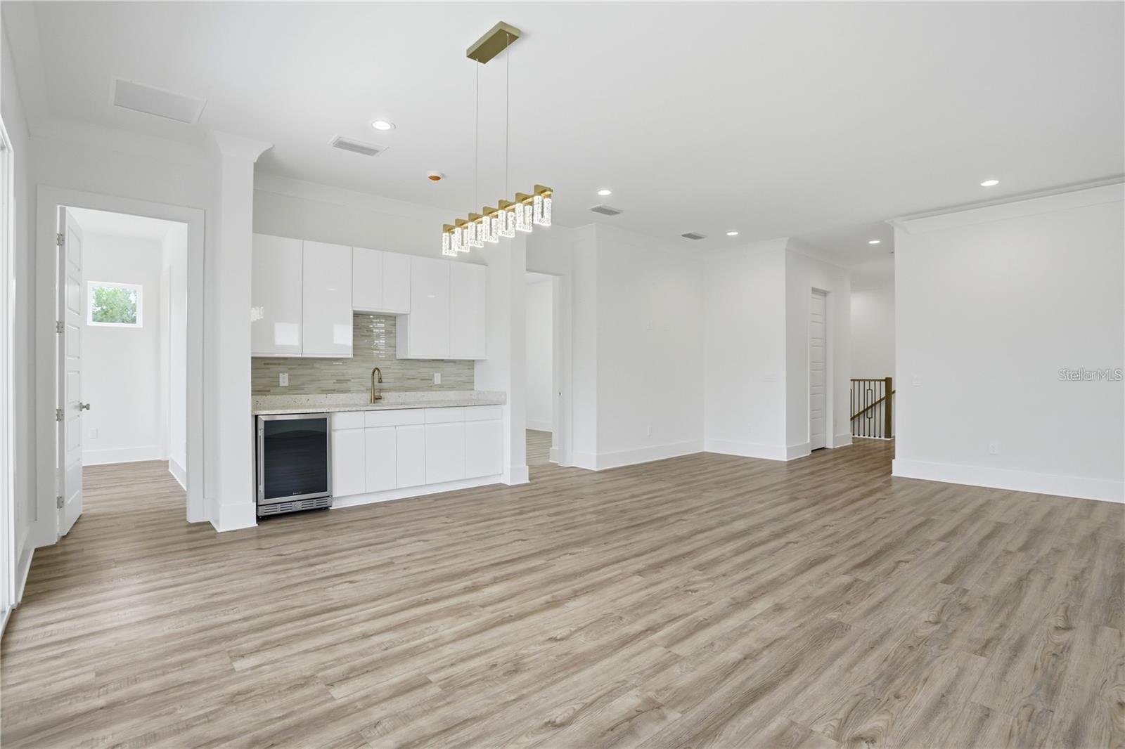Open, vacant kitchen with white cabinetry, a beverage refrigerator, and wood-look plank flooring.
