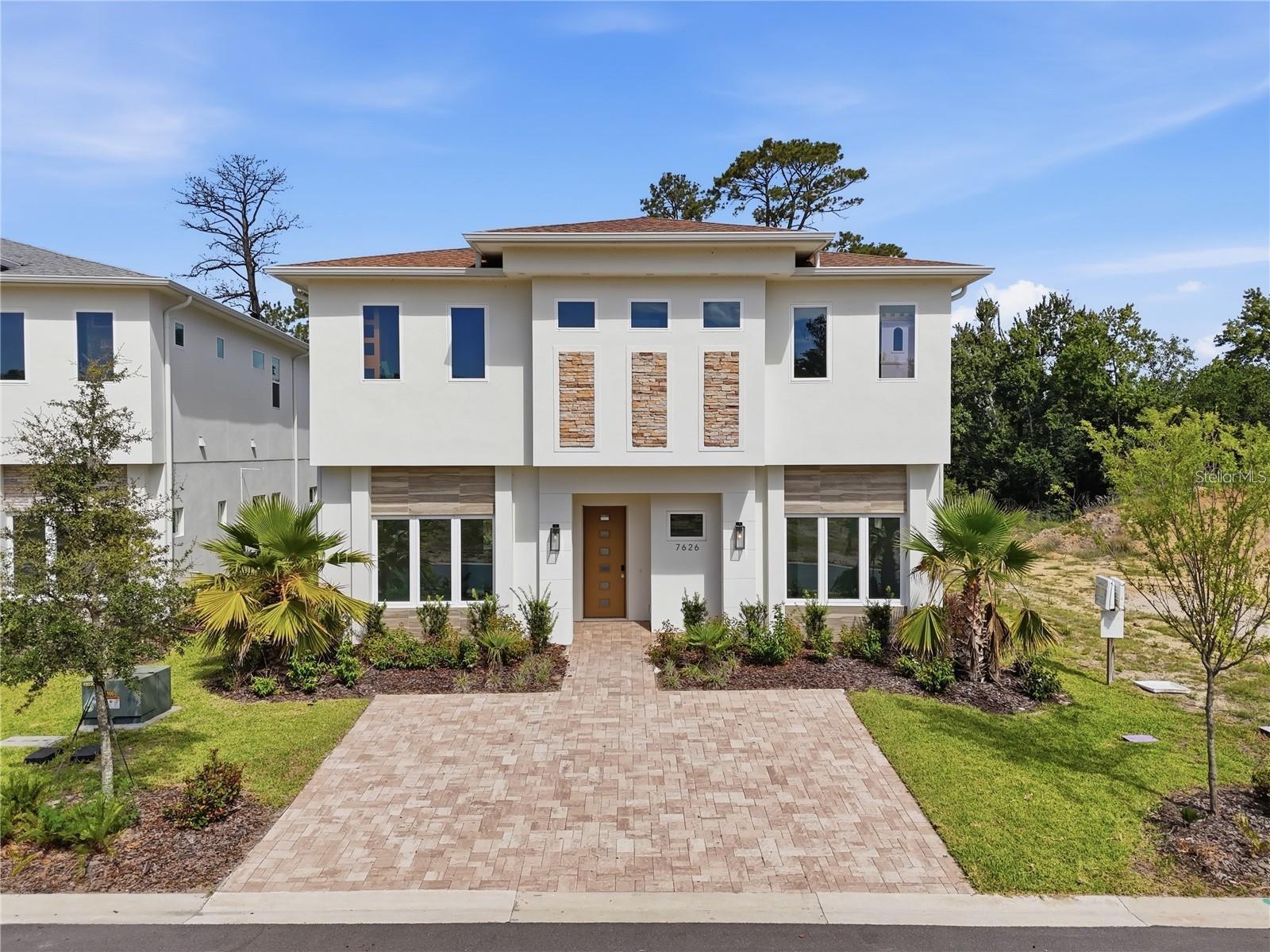 Modern two-story white home with stone accents, palm landscaping, and a wide paver driveway.