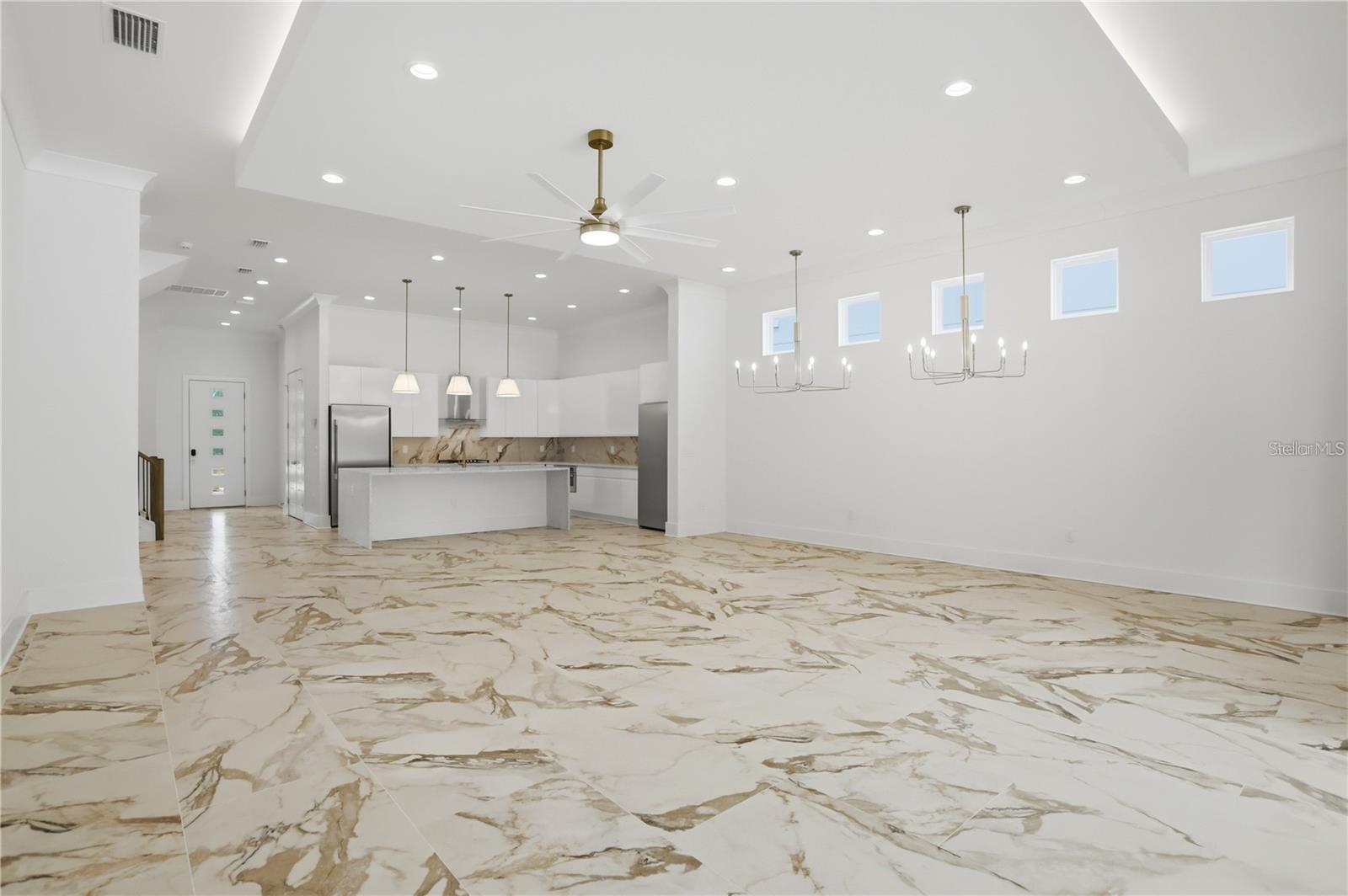 Open-plan kitchen with a white island, stainless appliances, high ceilings, and dramatic marble-look flooring.