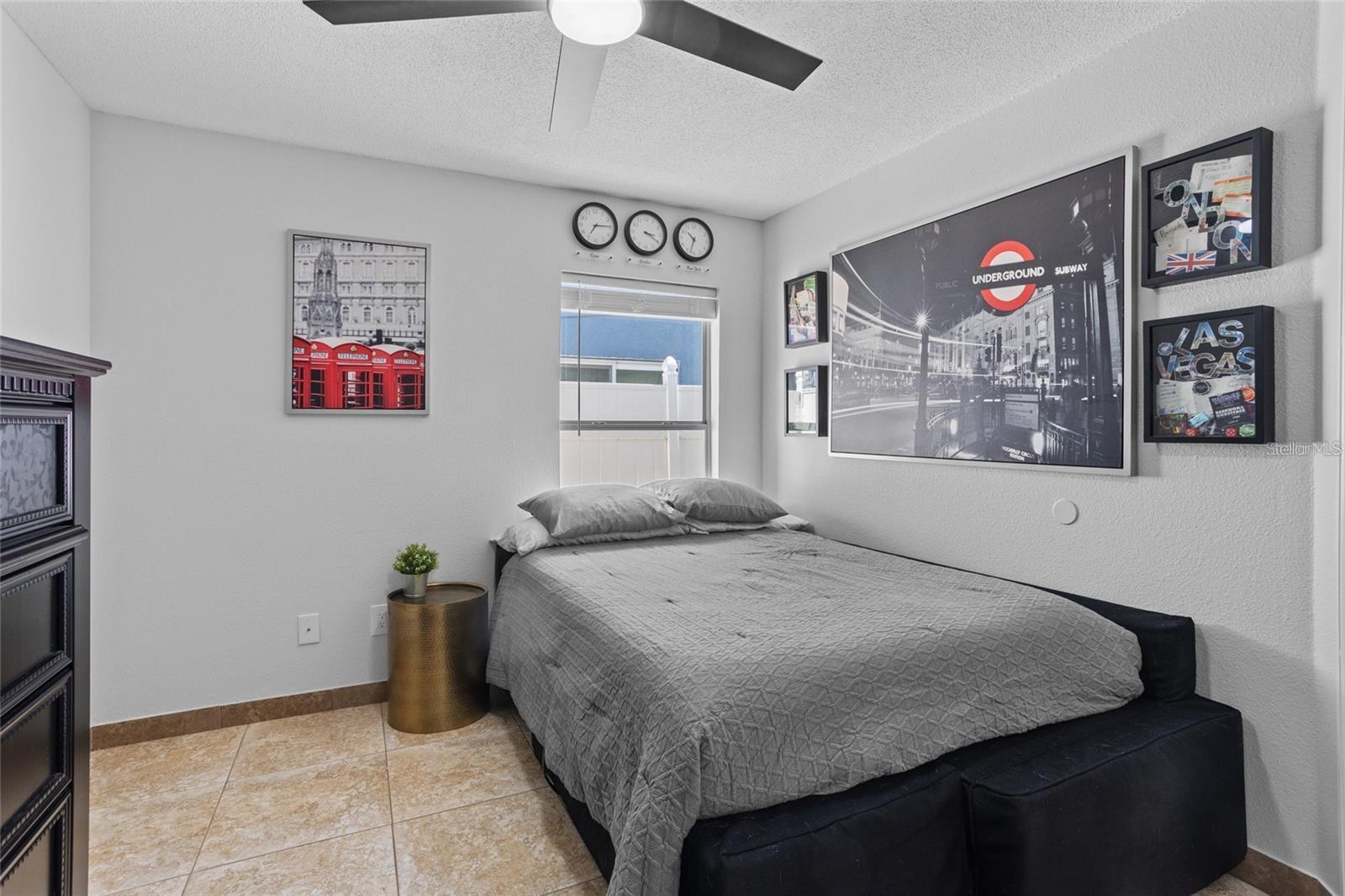 Bedroom with a gray quilted bed, tiled floor, and framed travel-themed wall art.
