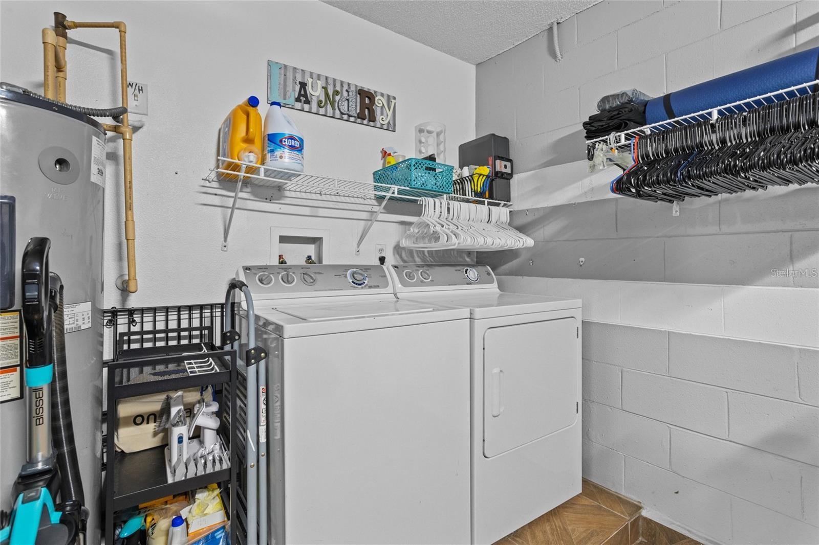Laundry room with a washer and dryer beneath storage shelves and hanging clothes hangers.