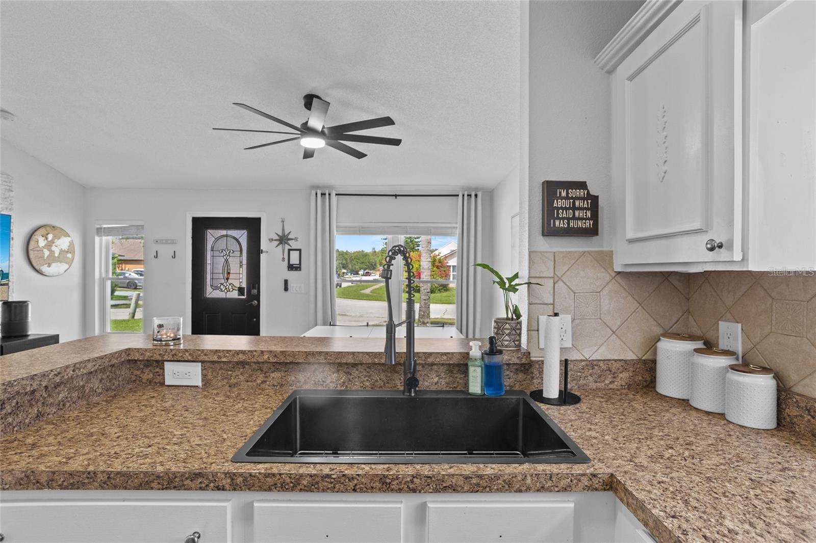 Kitchen with a granite peninsula, large black sink, and tan tiled backsplash.