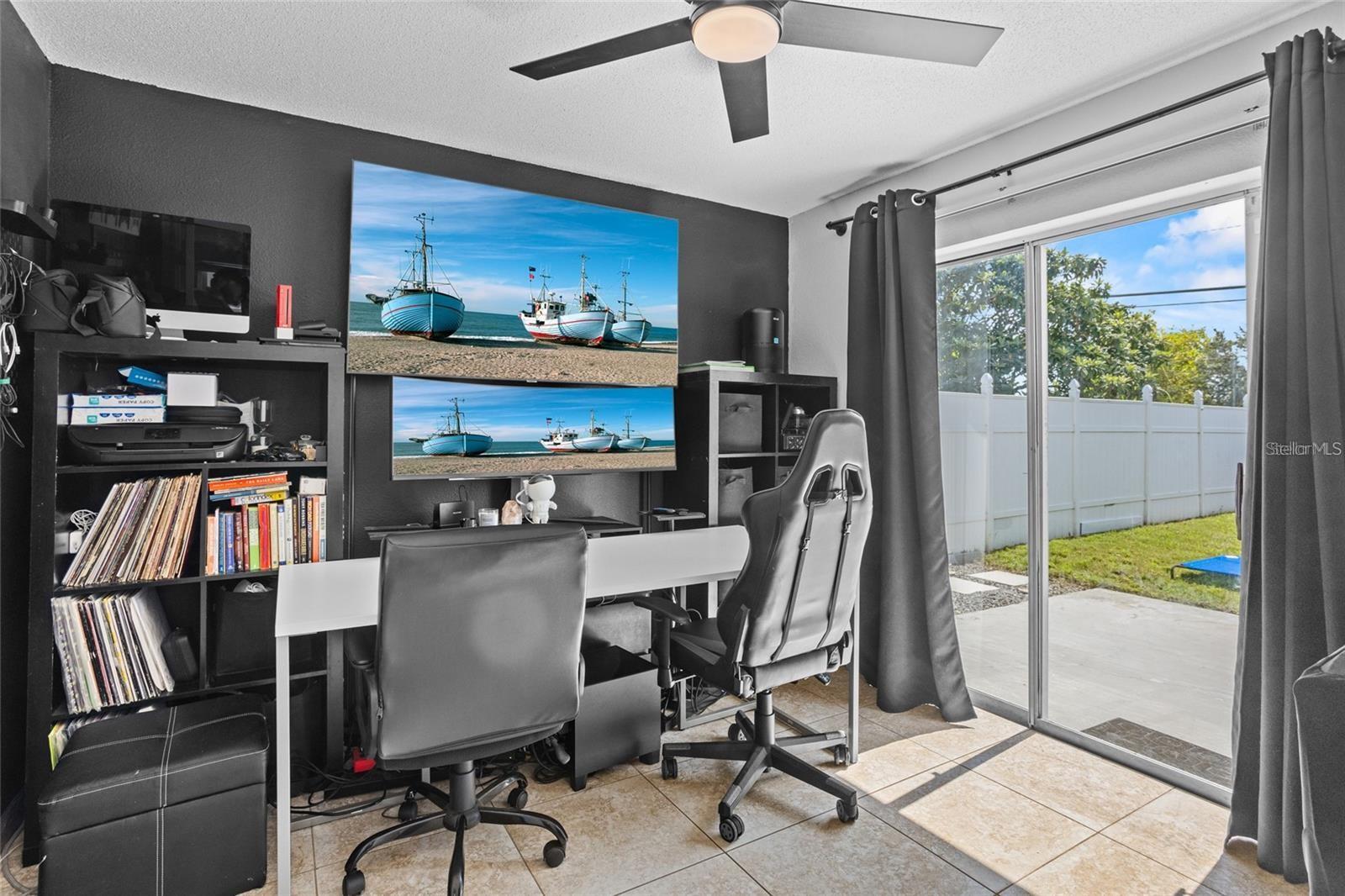Home office with two black chairs and sliding glass doors overlooking a fenced backyard.