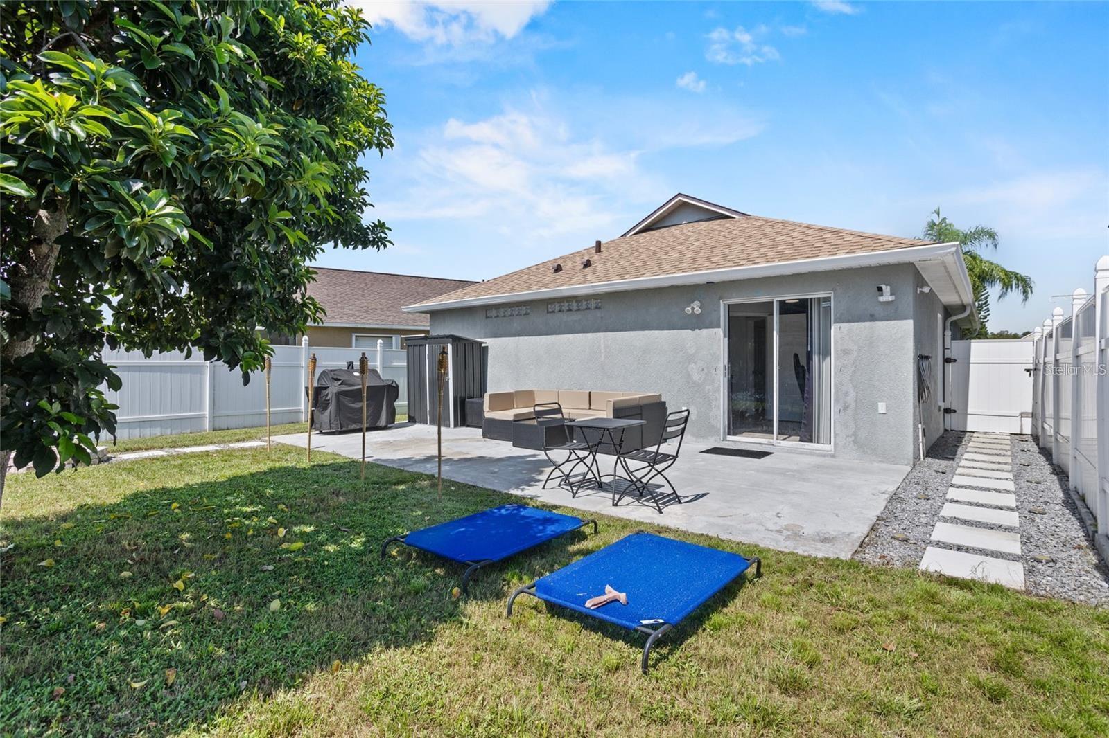 Backyard patio with outdoor seating beside a single-story home and white privacy fencing.