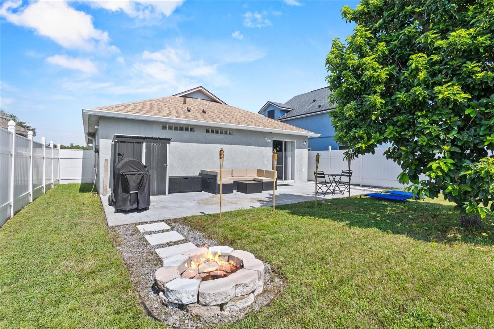 Fenced backyard with a patio, outdoor seating, grill, and stone fire pit.