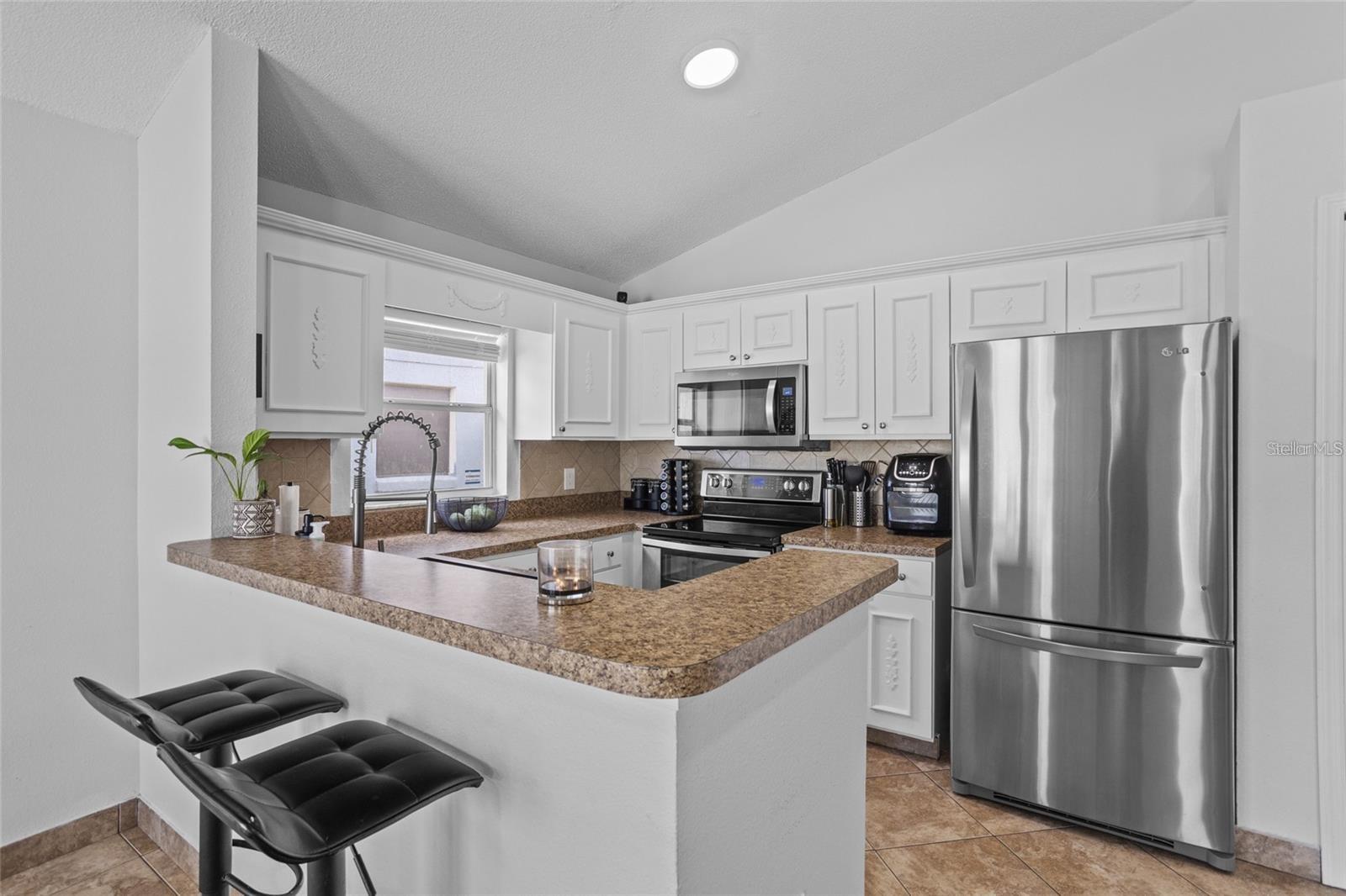 Kitchen with a stone-look breakfast bar, two stools, white cabinets, and stainless steel appliances.