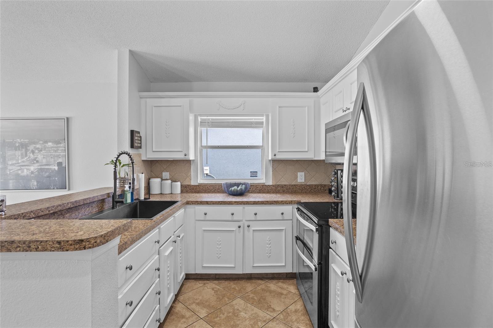 U-shaped kitchen with white cabinets, brown counters, stainless appliances, and tan tile flooring.