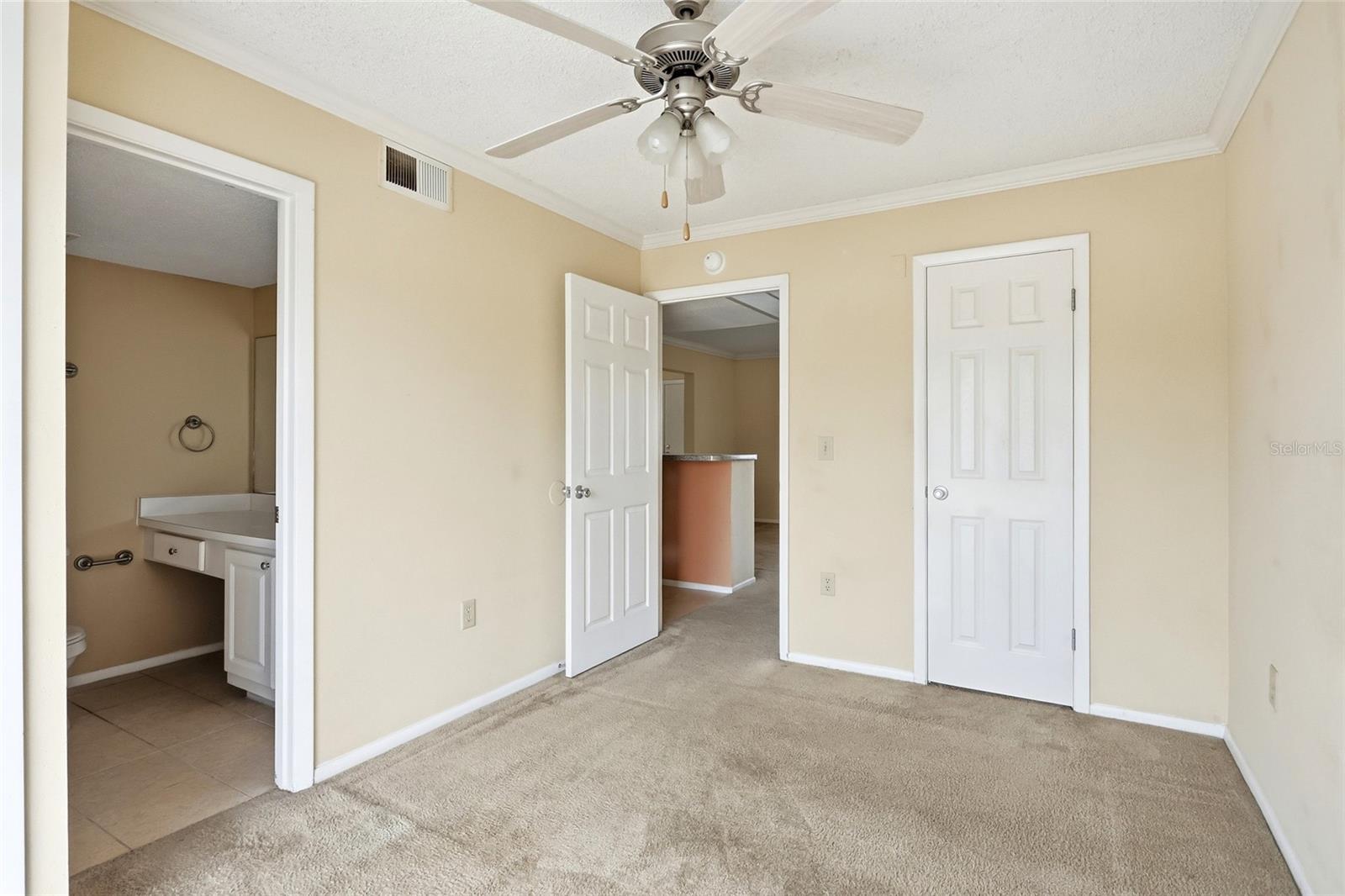 Unfurnished bedroom with beige carpet, ceiling fan, and an open doorway to the bathroom.