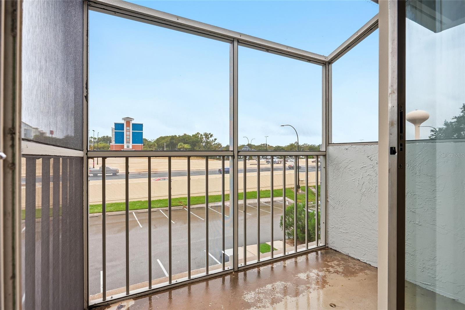 Screened balcony overlooking parking lots, a road, and a blue commercial building.