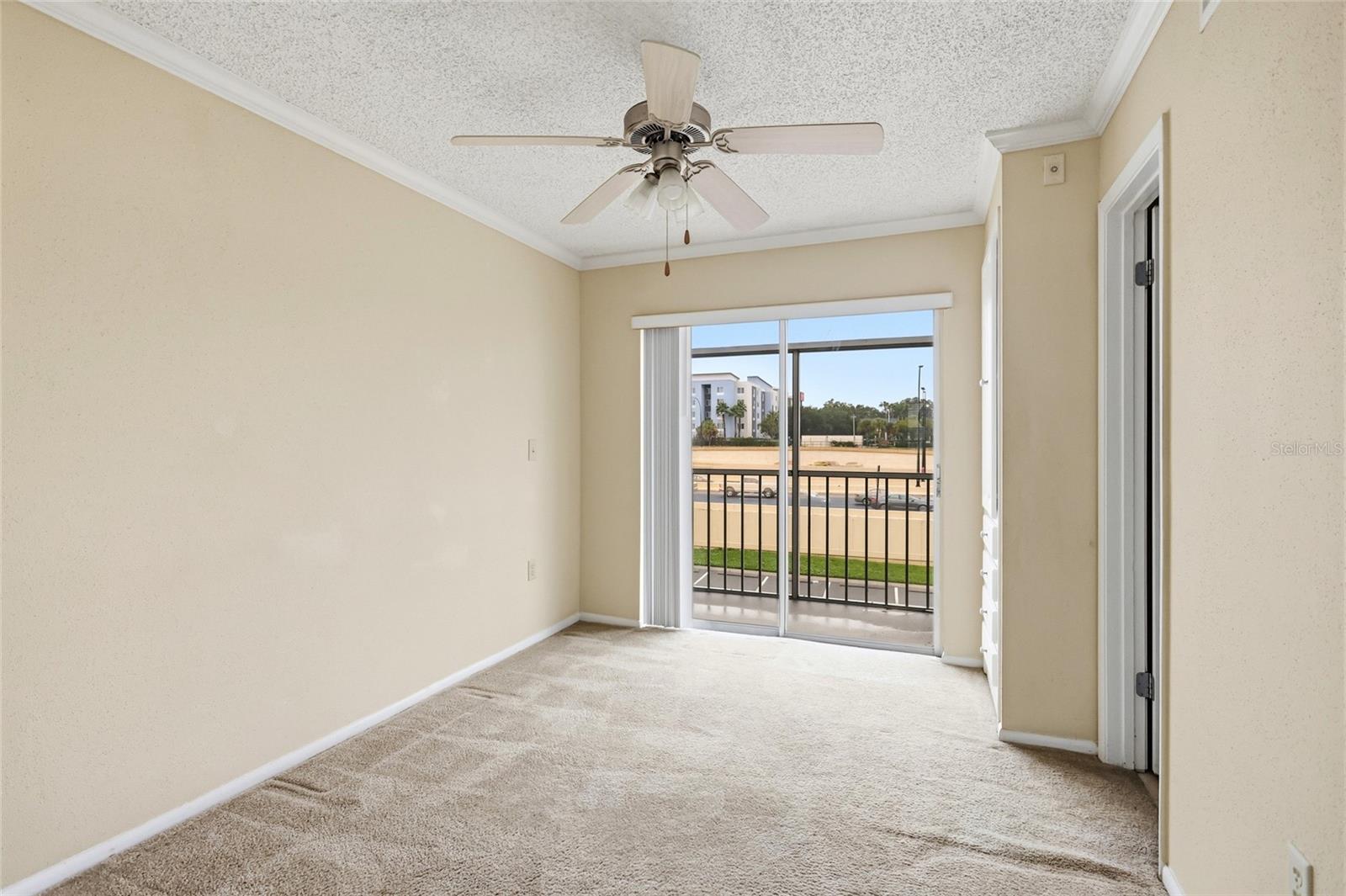 Vacant carpeted bedroom with a ceiling fan and sliding doors opening to a balcony.