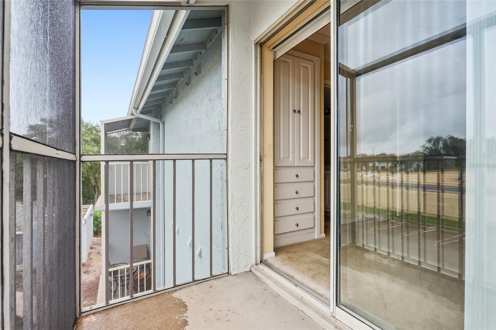Screened apartment balcony with metal railing and an open sliding glass door beside built-in drawers.