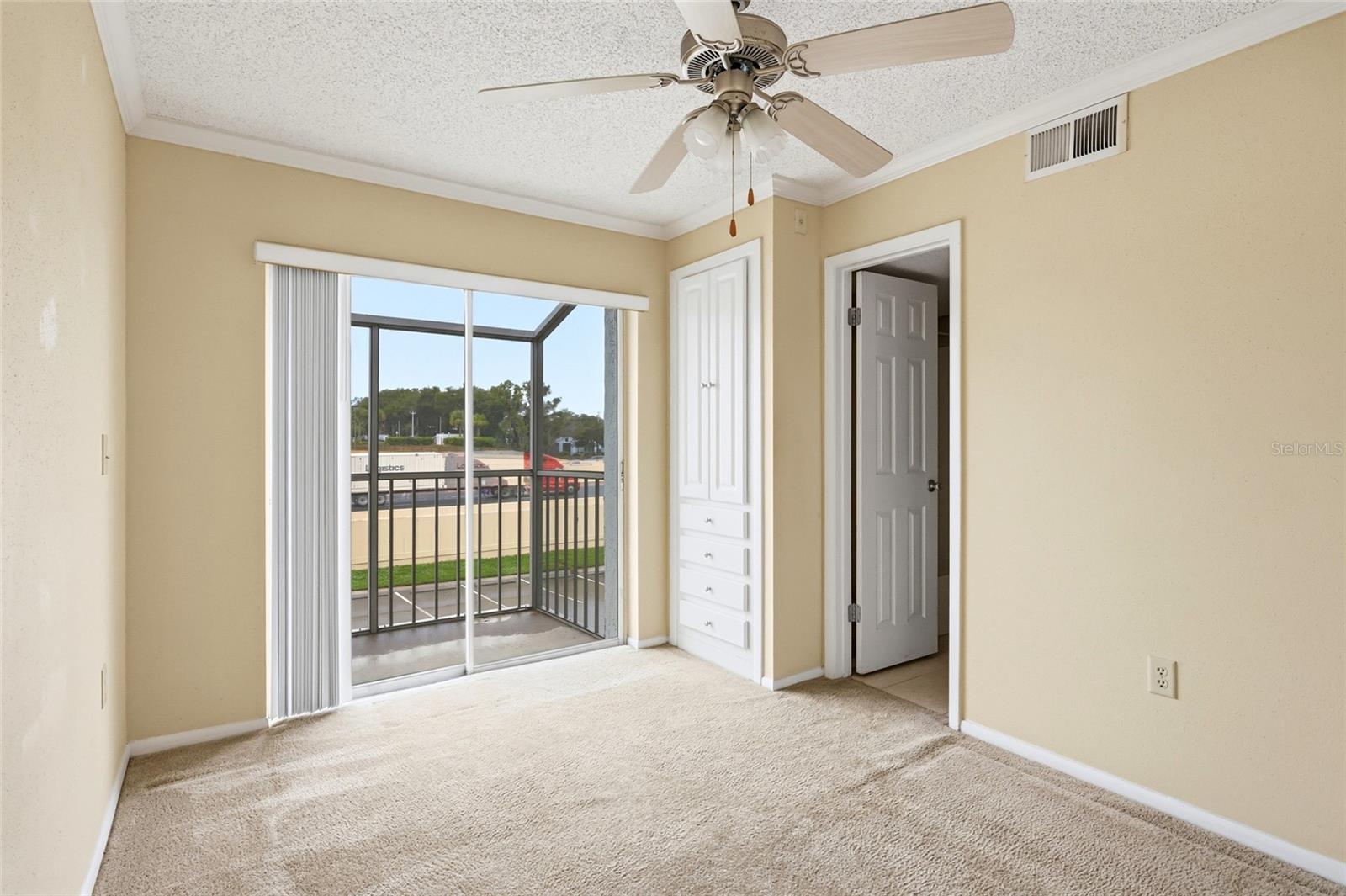 Empty carpeted bedroom with a ceiling fan, built-in closet, and sliding doors to a screened balcony.