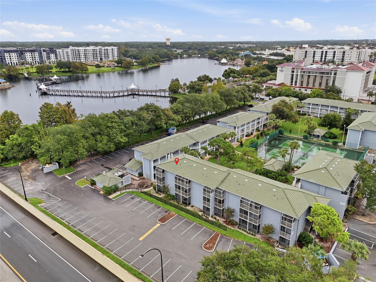 Aerial view of lakeside condominiums with a long pier and tennis courts.