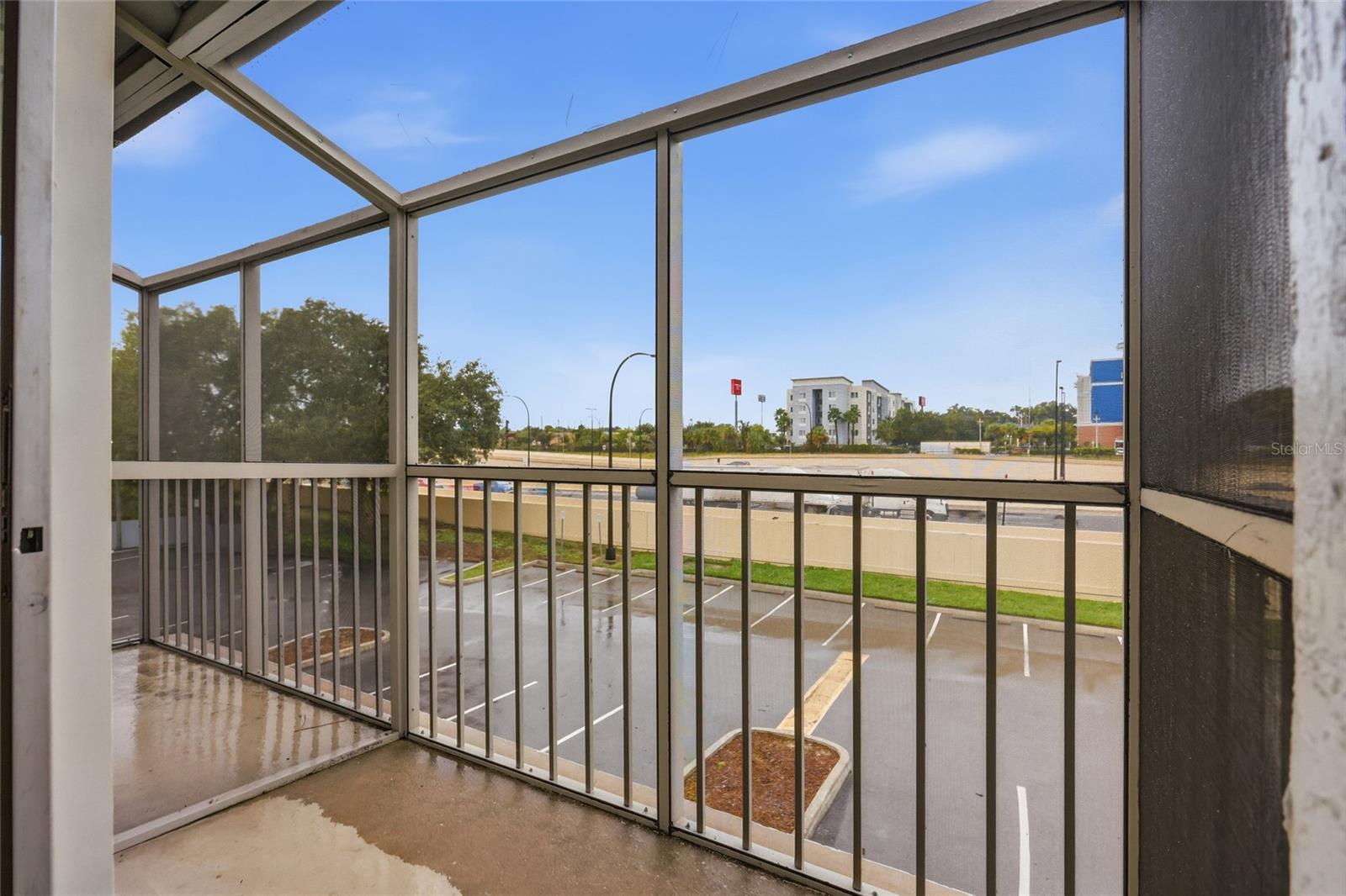 Screened-in balcony overlooking a parking lot and nearby buildings.