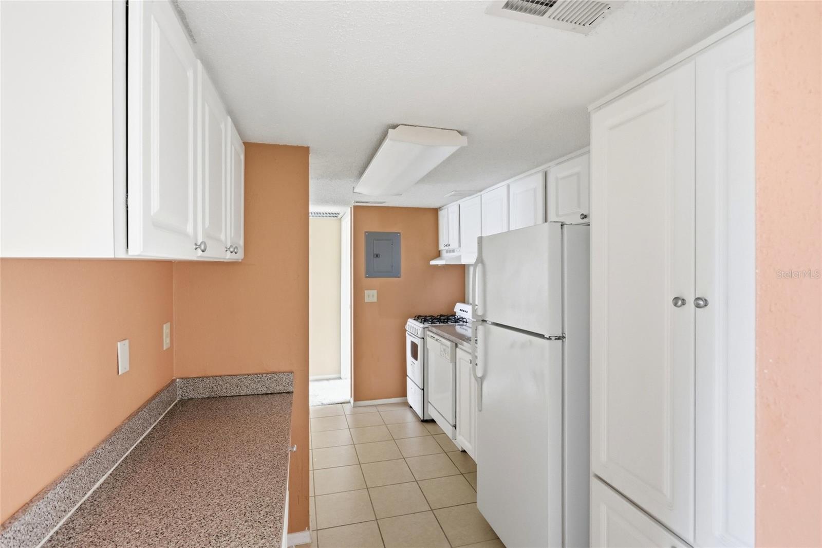 Galley kitchen with white cabinets, a speckled countertop, and white appliances.