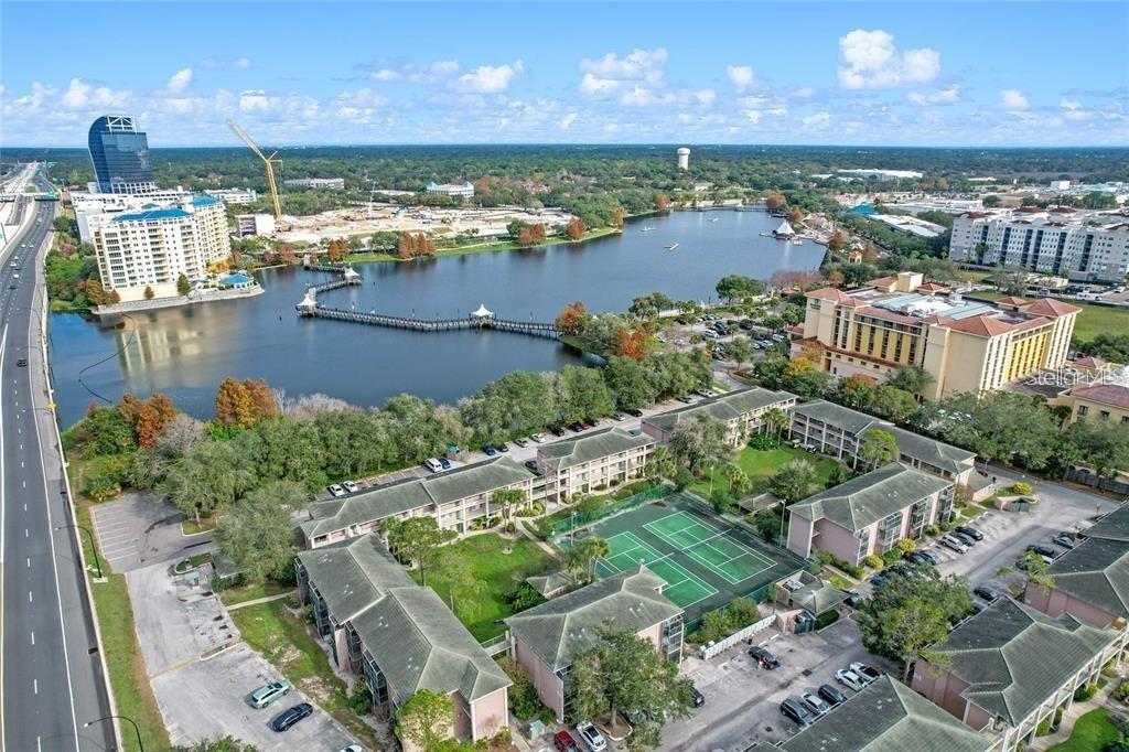 Aerial view of condominiums with tennis courts beside a lake and a long pier.
