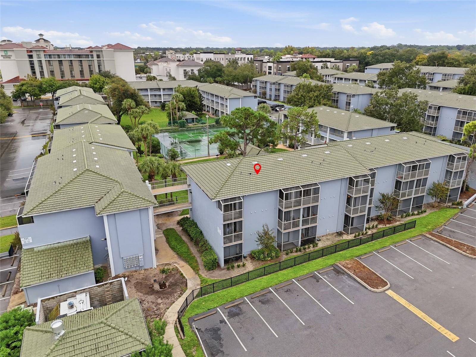 Aerial view of a condominium complex with a red marker on one building and a tennis court nearby.