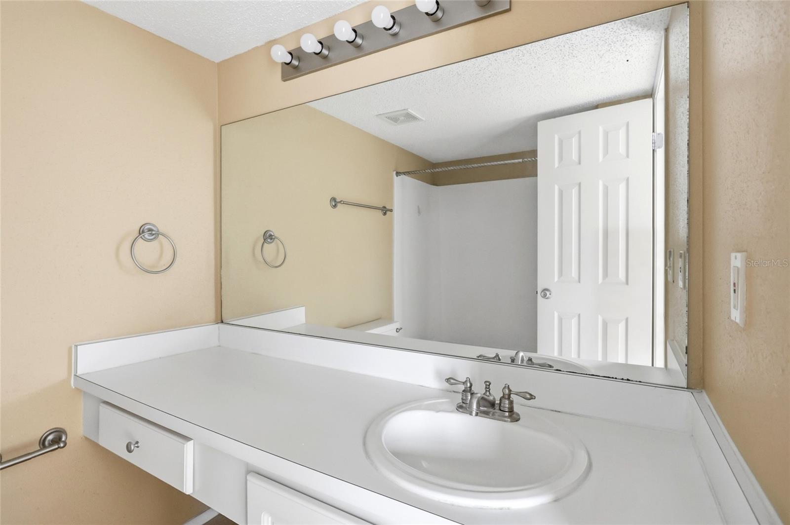 Bathroom vanity with an oval sink, wide mirror, and a row of lights above.