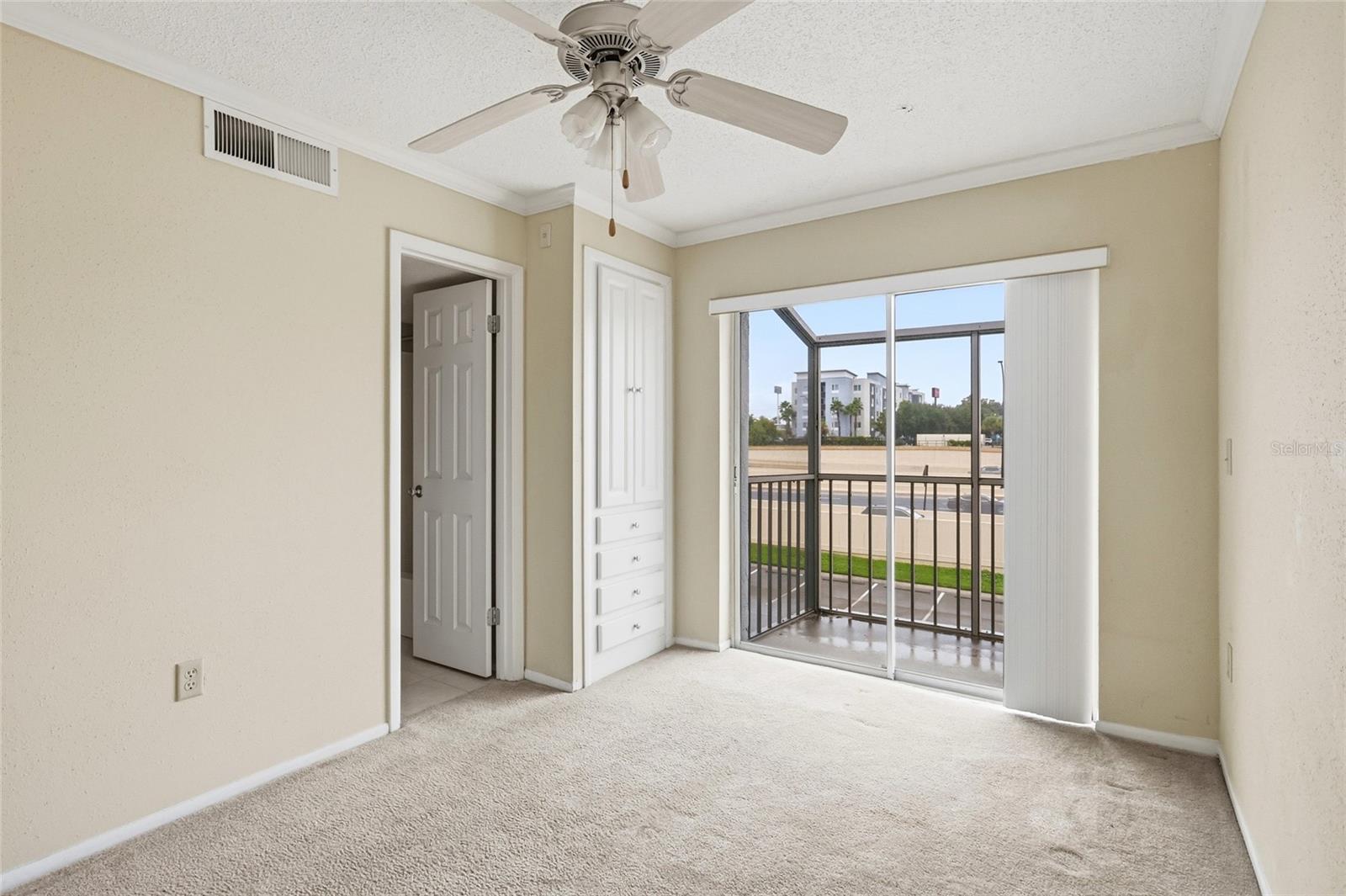 Empty bedroom with a ceiling fan, built-in drawers, and sliding doors to a screened balcony.