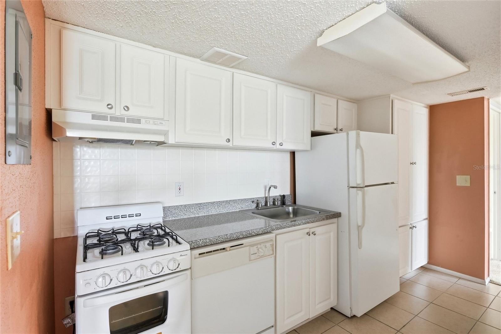 Kitchen with white cabinets, gas range, refrigerator, and gray speckled countertops.