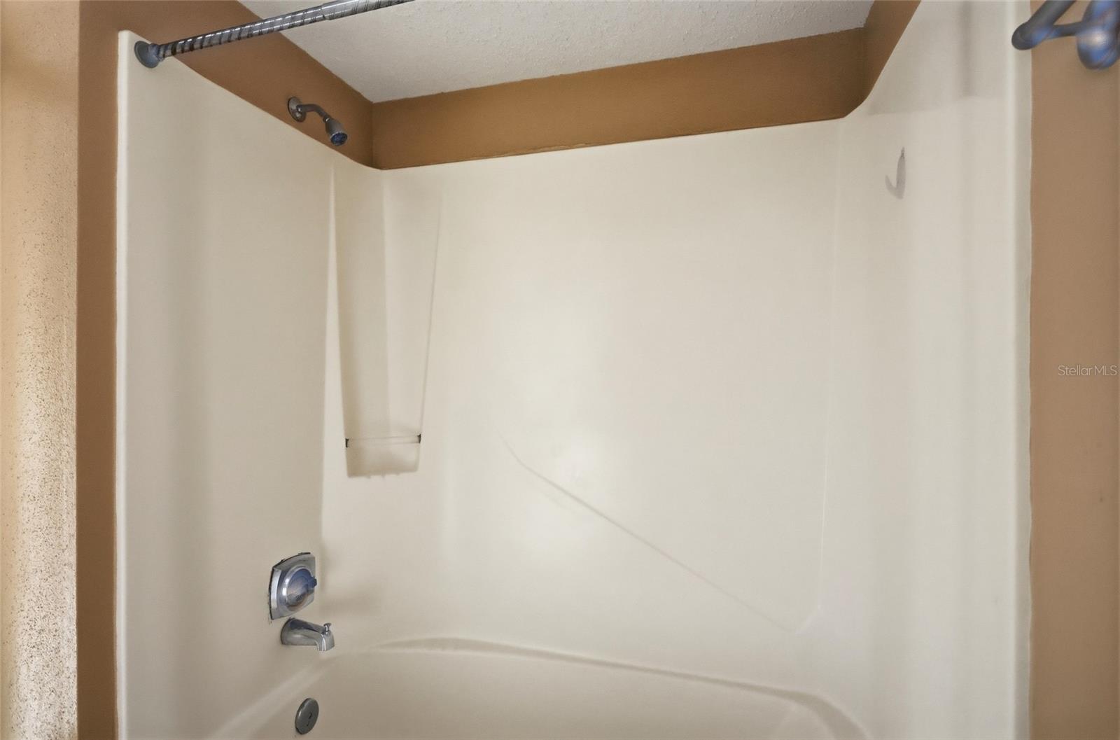 White bathtub and shower enclosure with chrome fixtures and a built-in shelf.