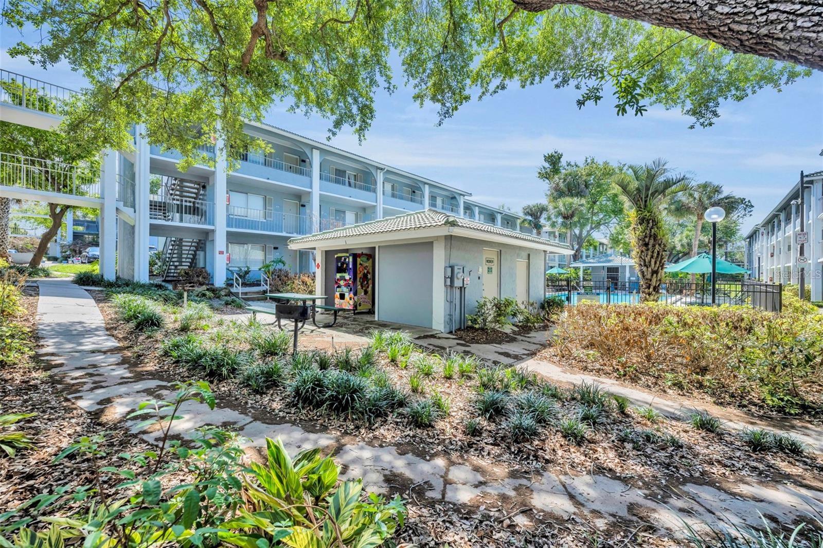 Condominium complex with exterior balconies, landscaped walkways, and a fenced pool.