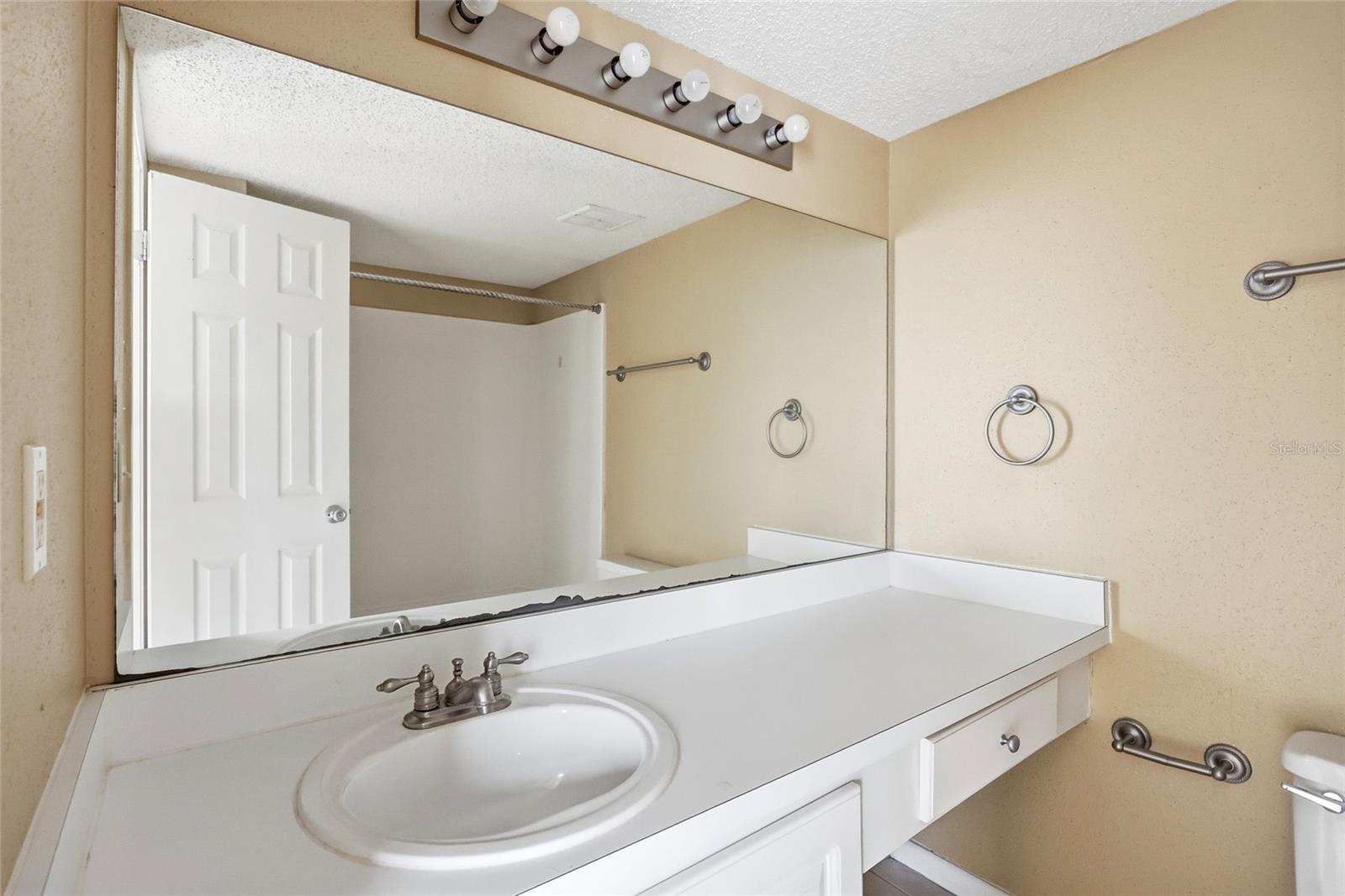 Bathroom vanity with an oval sink, large mirror, and chrome towel bars.