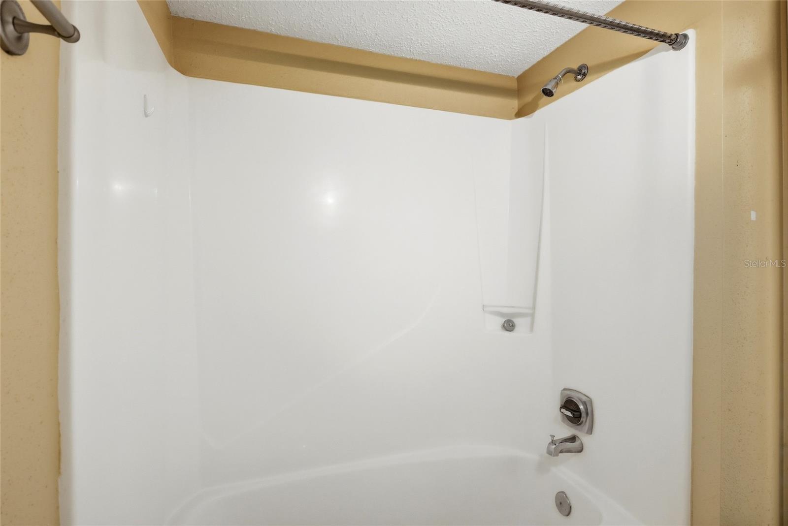 White bathtub and shower with chrome fixtures and a recessed soap shelf.