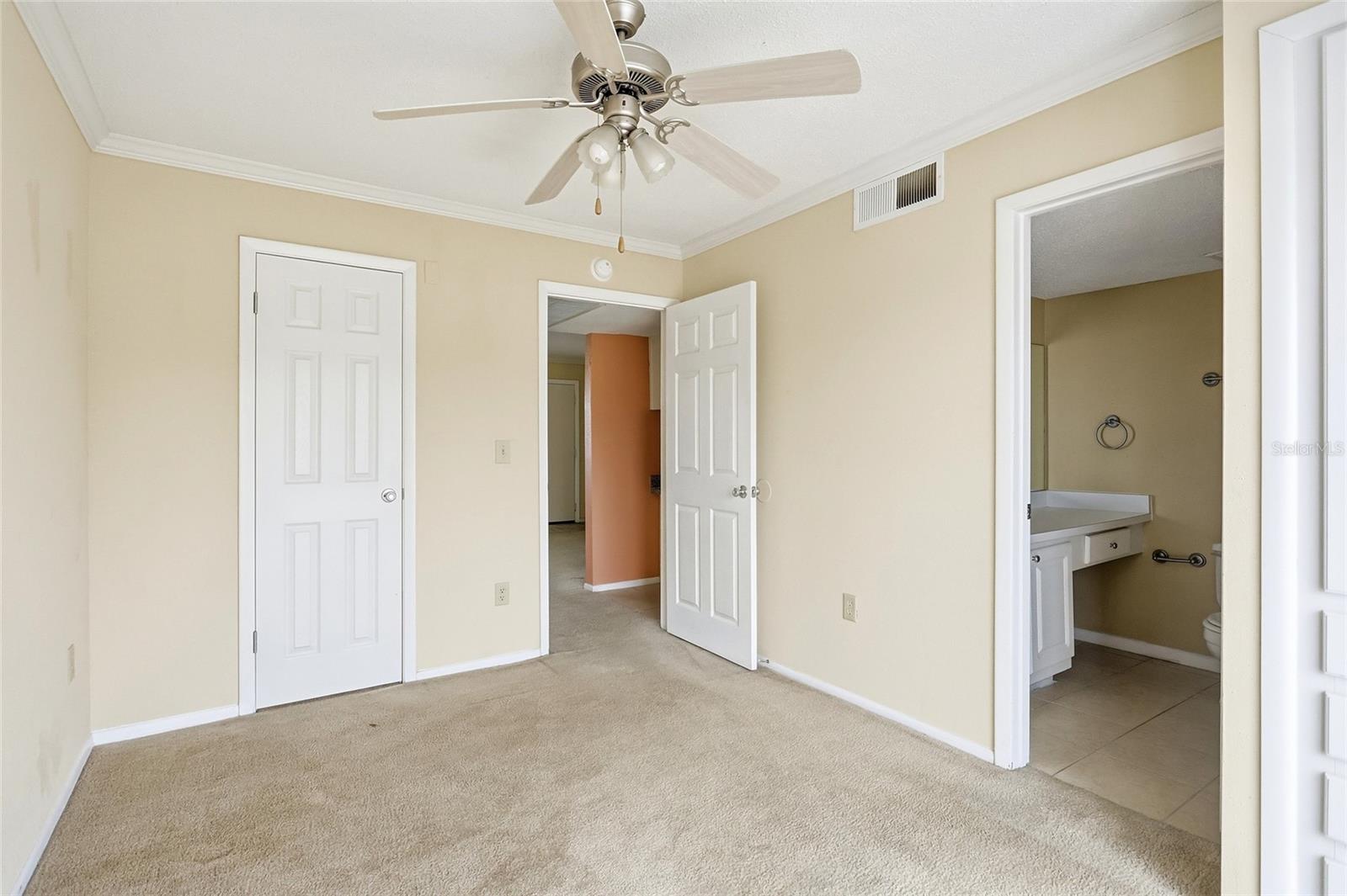 Unfurnished bedroom with beige carpet, ceiling fan, and adjoining bathroom.