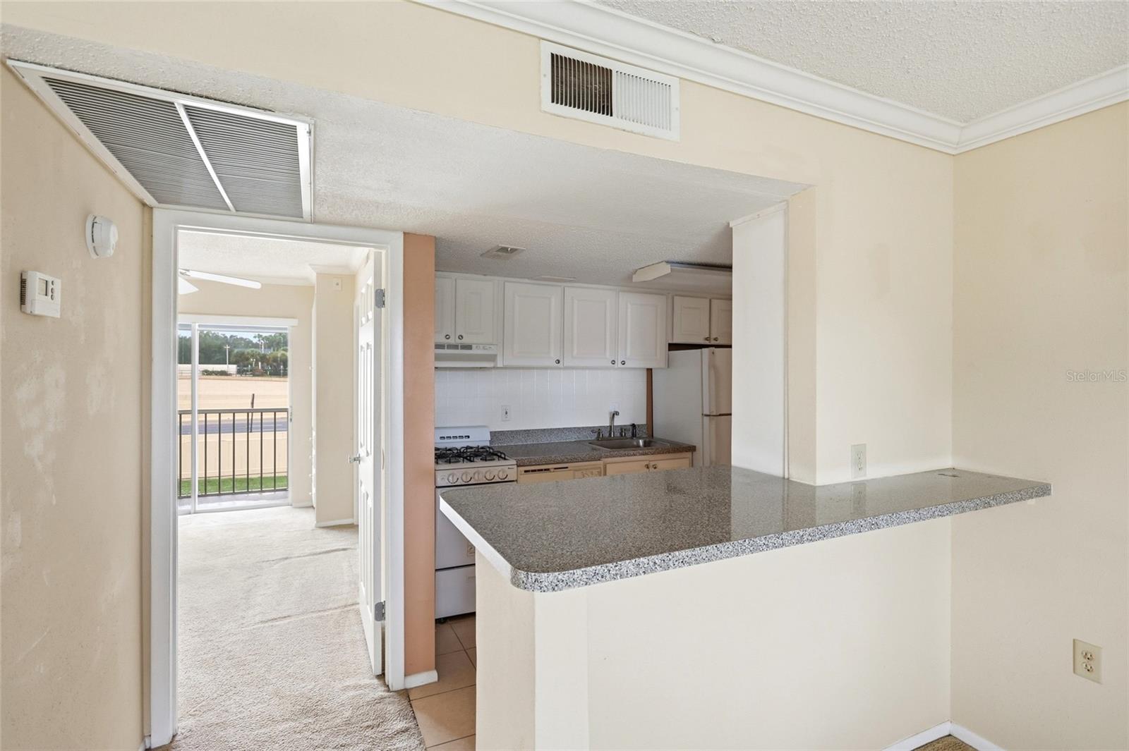 Vacant condo kitchen with white cabinets and a speckled breakfast bar beside an open doorway to a balcony.
