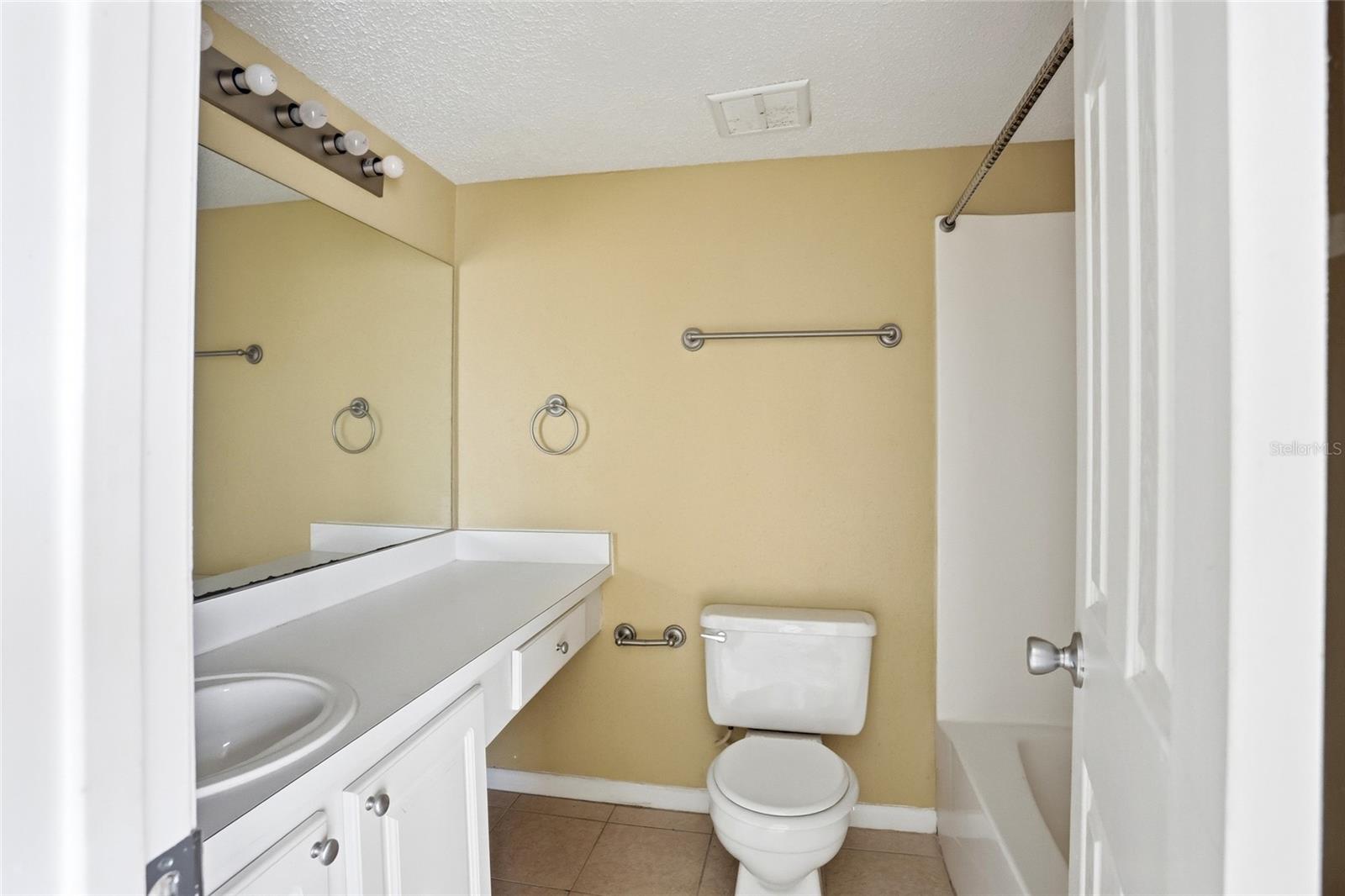 Bathroom with a white vanity and large mirror beside a toilet and curtained bathtub.