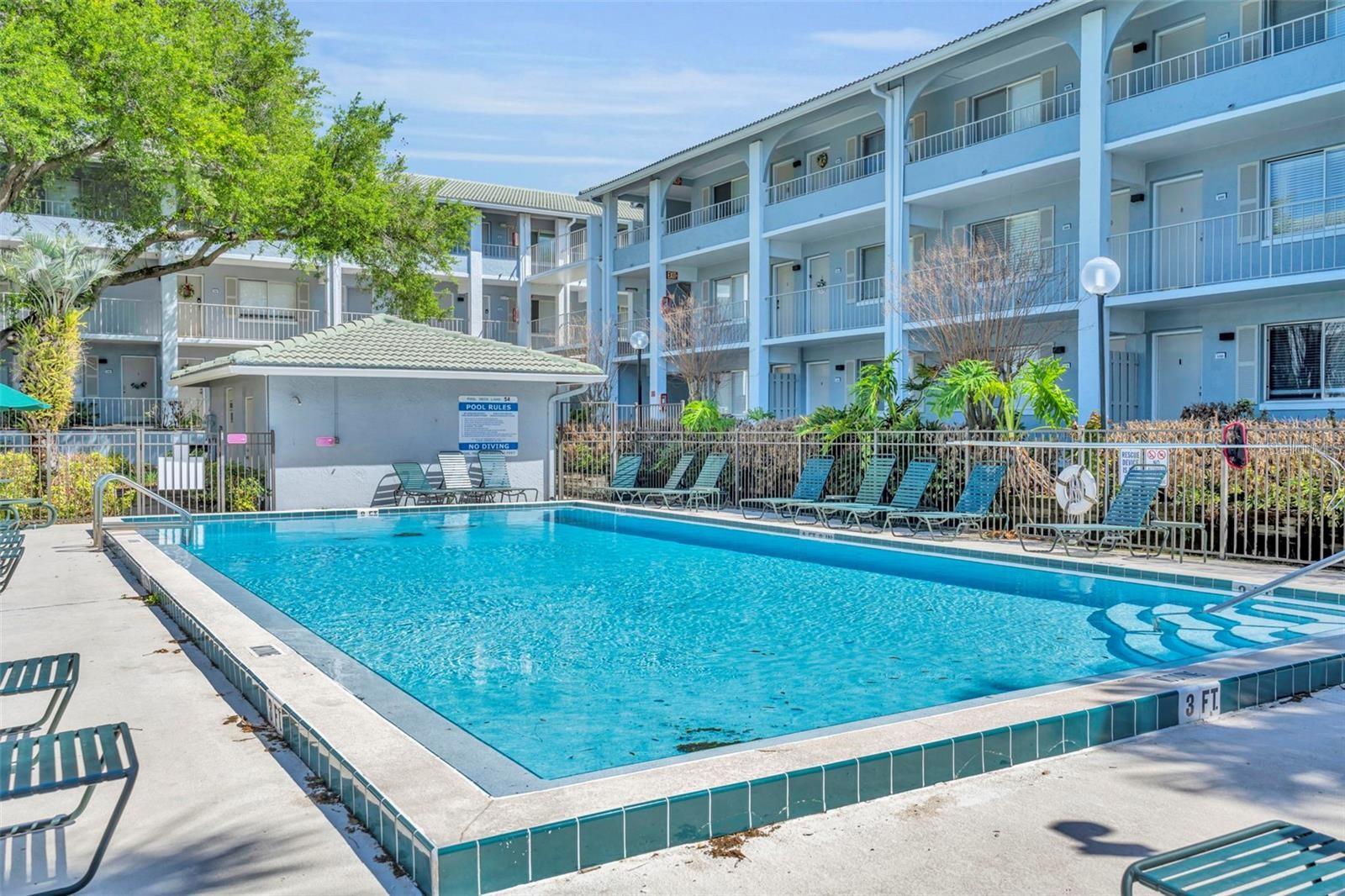 Outdoor swimming pool with lounge chairs in front of a blue condominium building.