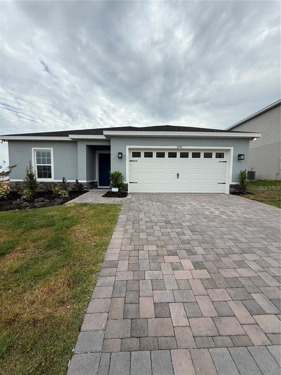 Single-story gray house with a white double garage and broad paver driveway.