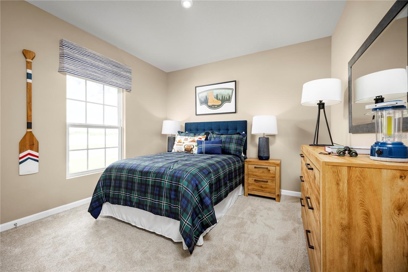 Bedroom with a blue plaid bed, large window, and wood dresser.