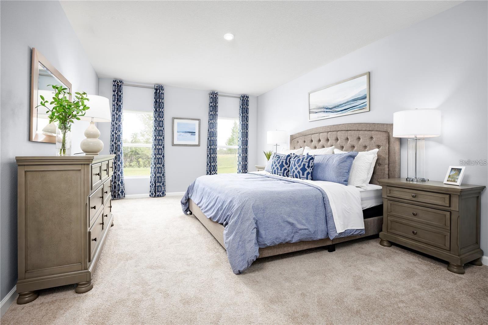 Staged bedroom with a tufted bed, blue-and-white bedding, matching wood furniture, and two curtained windows.