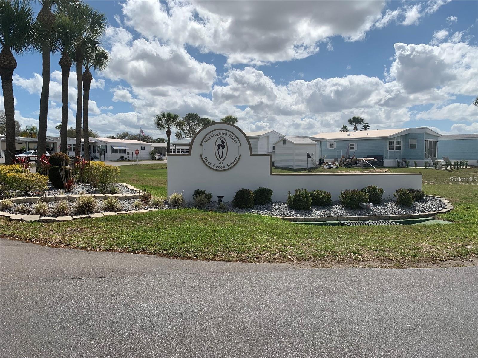 Mockingbird Ridge at Deer Creek Resort entrance sign, with palms and manufactured homes behind it.