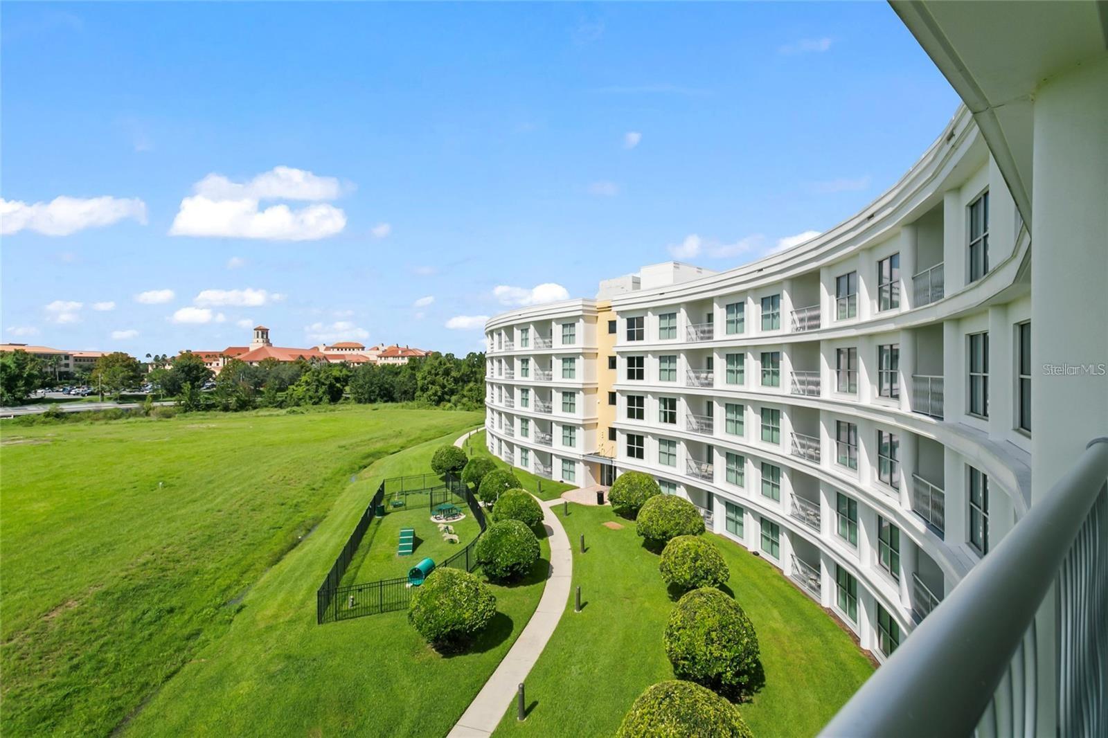 Curved white condominium building overlooking landscaped grounds, a walking path, and open green space.