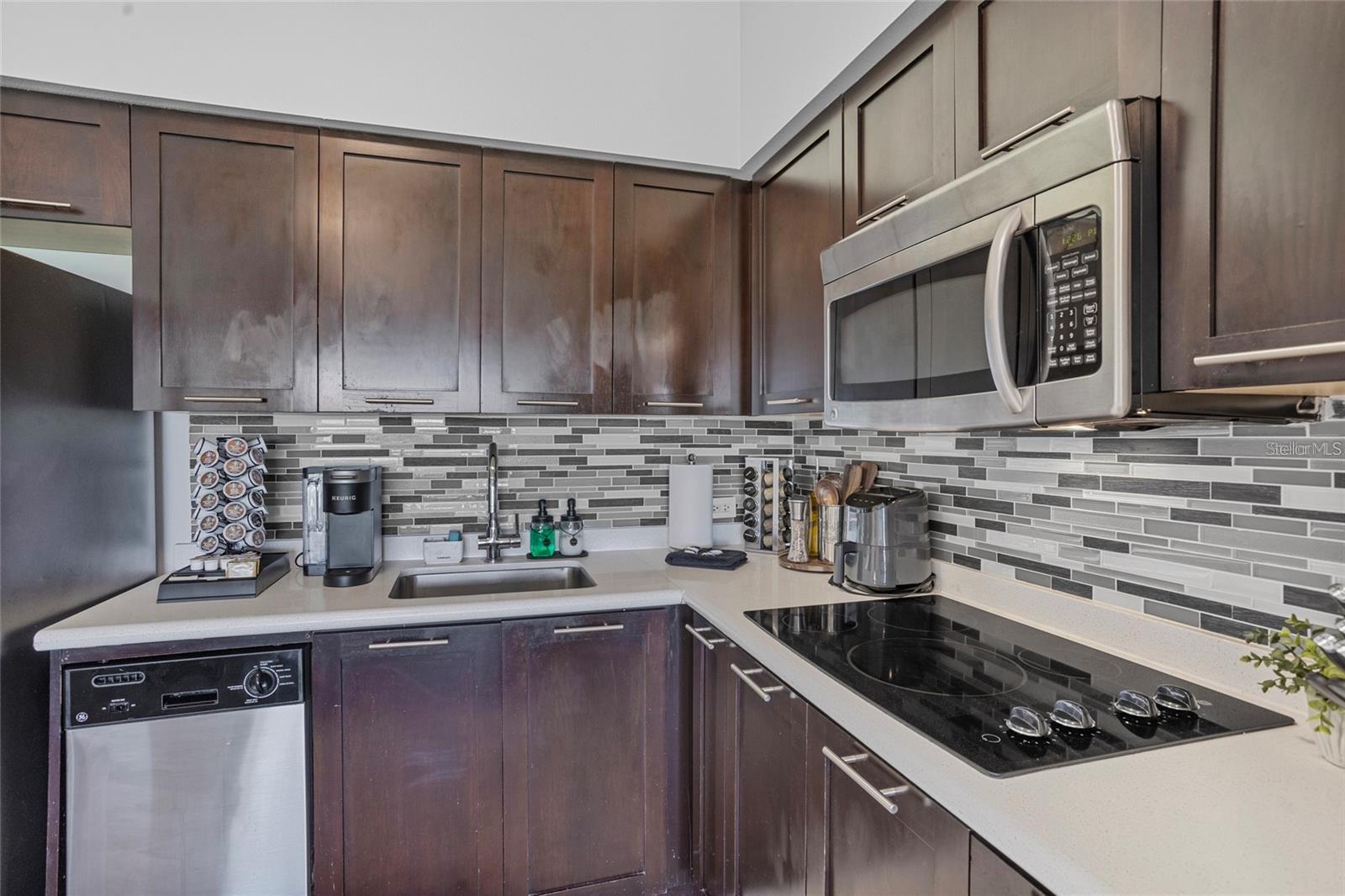 Kitchen with dark wood cabinets, mosaic tile backsplash, stainless steel appliances, and a black glass cooktop.