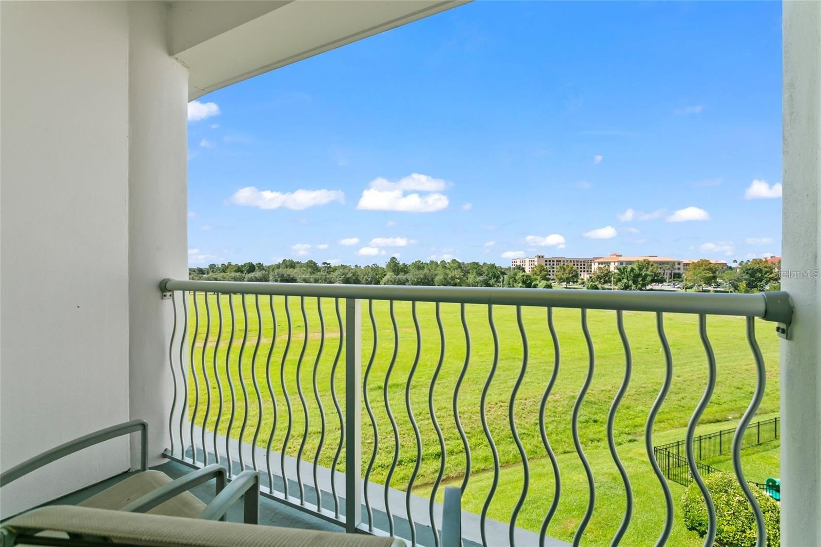 Covered balcony overlooking a green field, trees, and distant buildings.